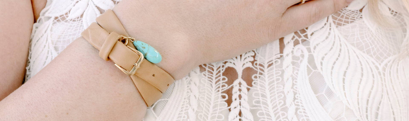 Close up of woman's wrist wearing bracelet with a tan leather strap and turquoise charm