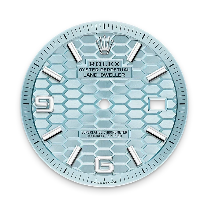 Close-up of a light blue Rolex Land-Dweller watch dial with silver hour markers, the Rolex crown logo at the top, and a date window on the right side.