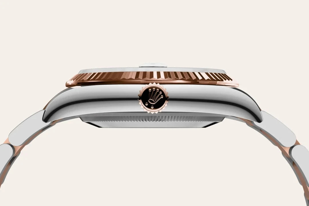 Side profile of a luxury watch featuring a polished silver case, a rose gold bezel with textured detailing, and a crown engraved with a stylized emblem.