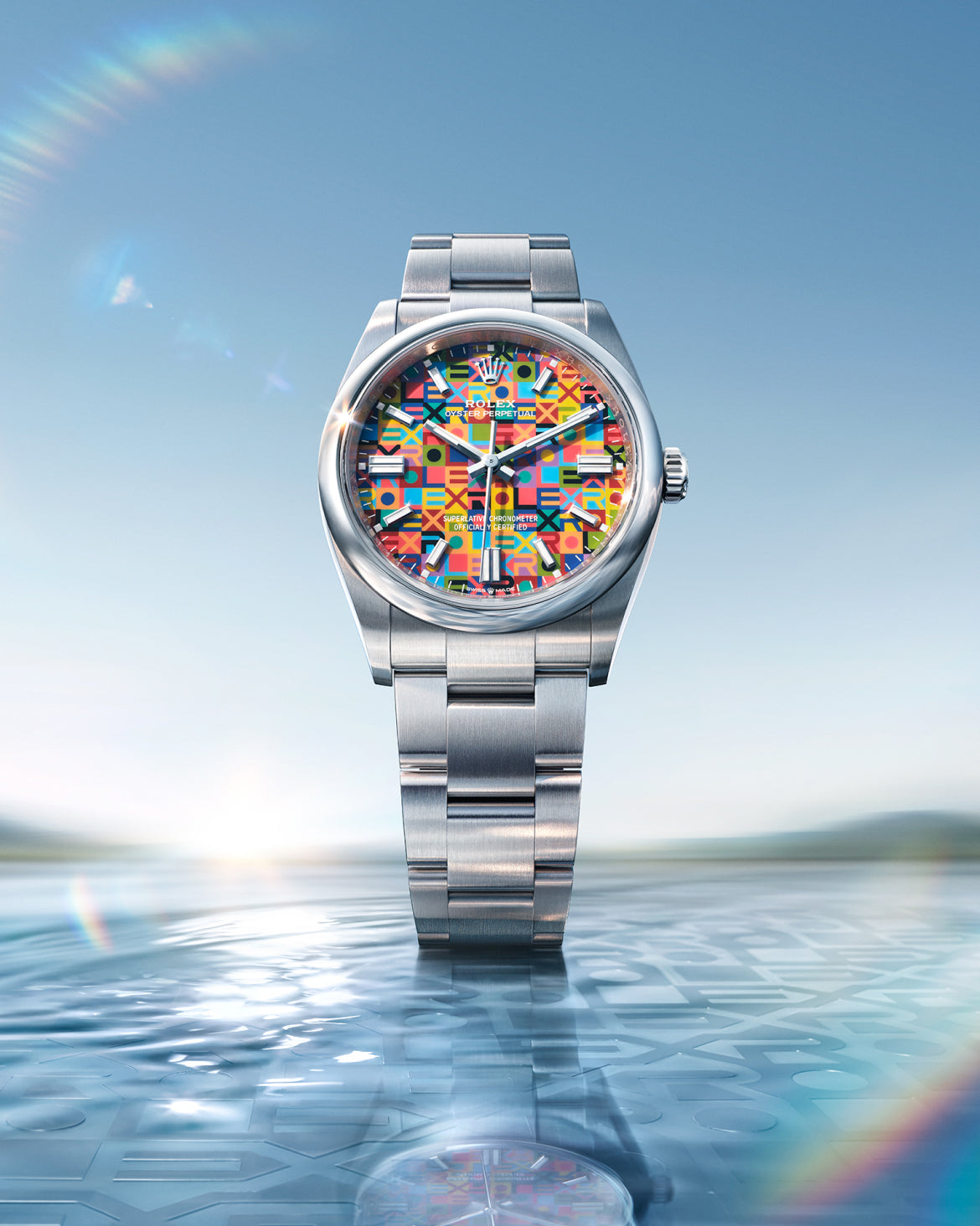 Silver luxury watch with a colorful geometric pattern on the dial, displayed above a reflective surface with soft lighting and a clear blue sky background.