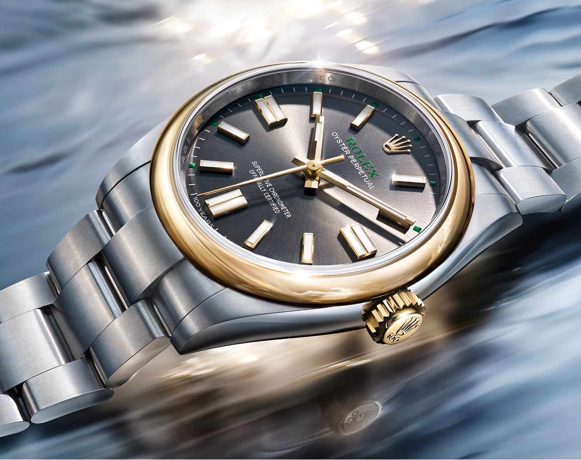 Close-up of a luxury Rolex watch with a gold bezel and a stainless steel bracelet resting on a reflective, flowing surface, highlighting fine craftsmanship and design.