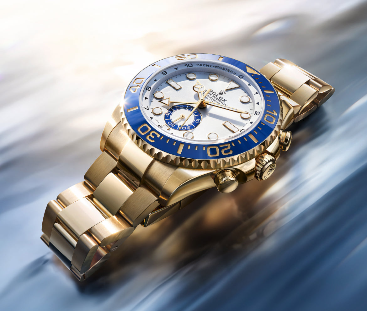 Close-up of a gold luxury wristwatch with a white dial and blue bezel, showcasing polished metal links and detailed craftsmanship in soft natural light.
