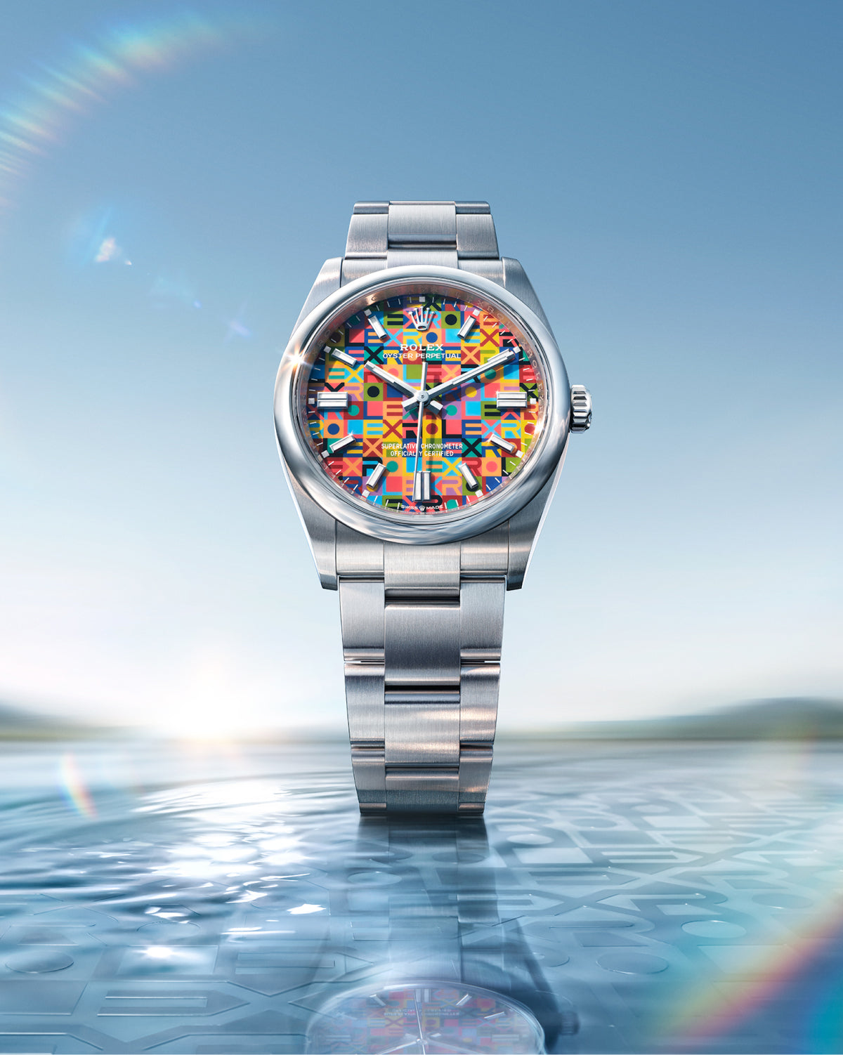 Rolex luxury watch with a multicolored geometric patterned dial and stainless steel bracelet, standing upright on a reflective water surface under a clear sky.