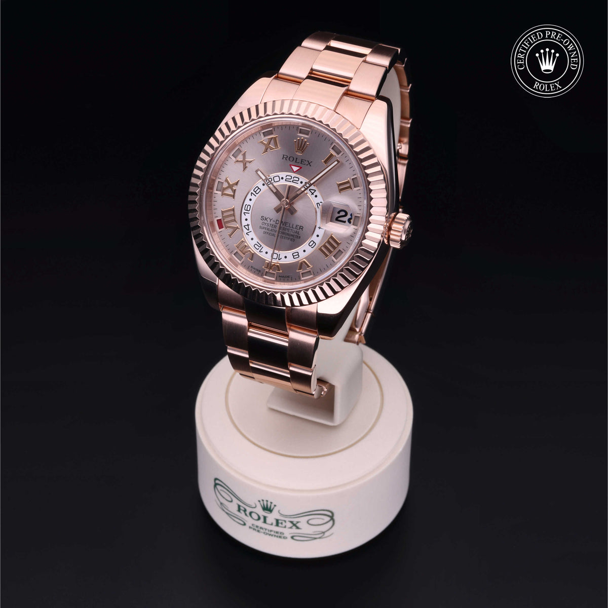 Rose gold Rolex watch with a silver dial and Roman numerals on a white stand featuring the Rolex logo, displaying luxury craftsmanship and timeless design.