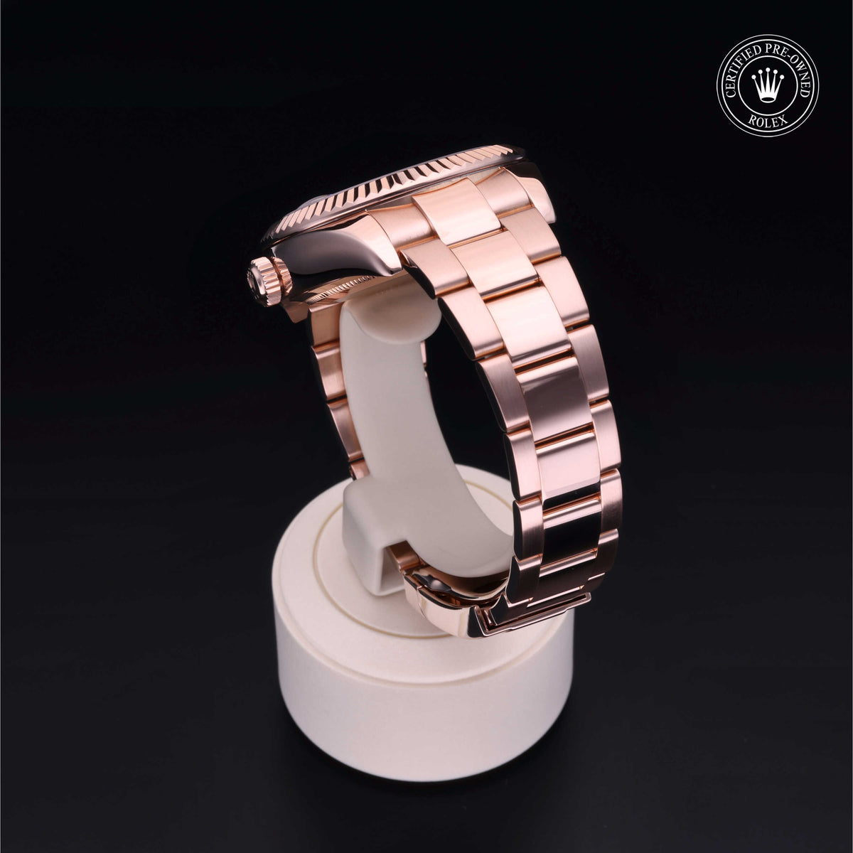 Rose gold Rolex watch band displayed on a white stand with a certified pre-owned Rolex logo on a black background, highlighting luxury watch craftsmanship.