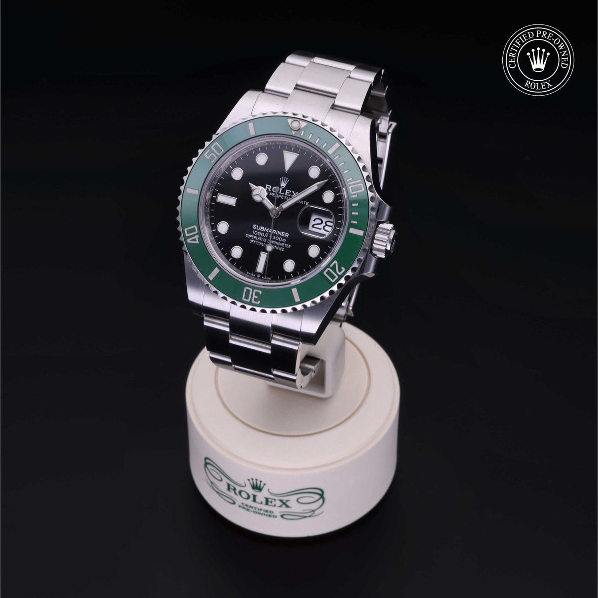 Rolex stainless steel watch with a green bezel and black dial displayed on a branded stand, featuring a date window and Certified Pre-Owned Rolex logo.