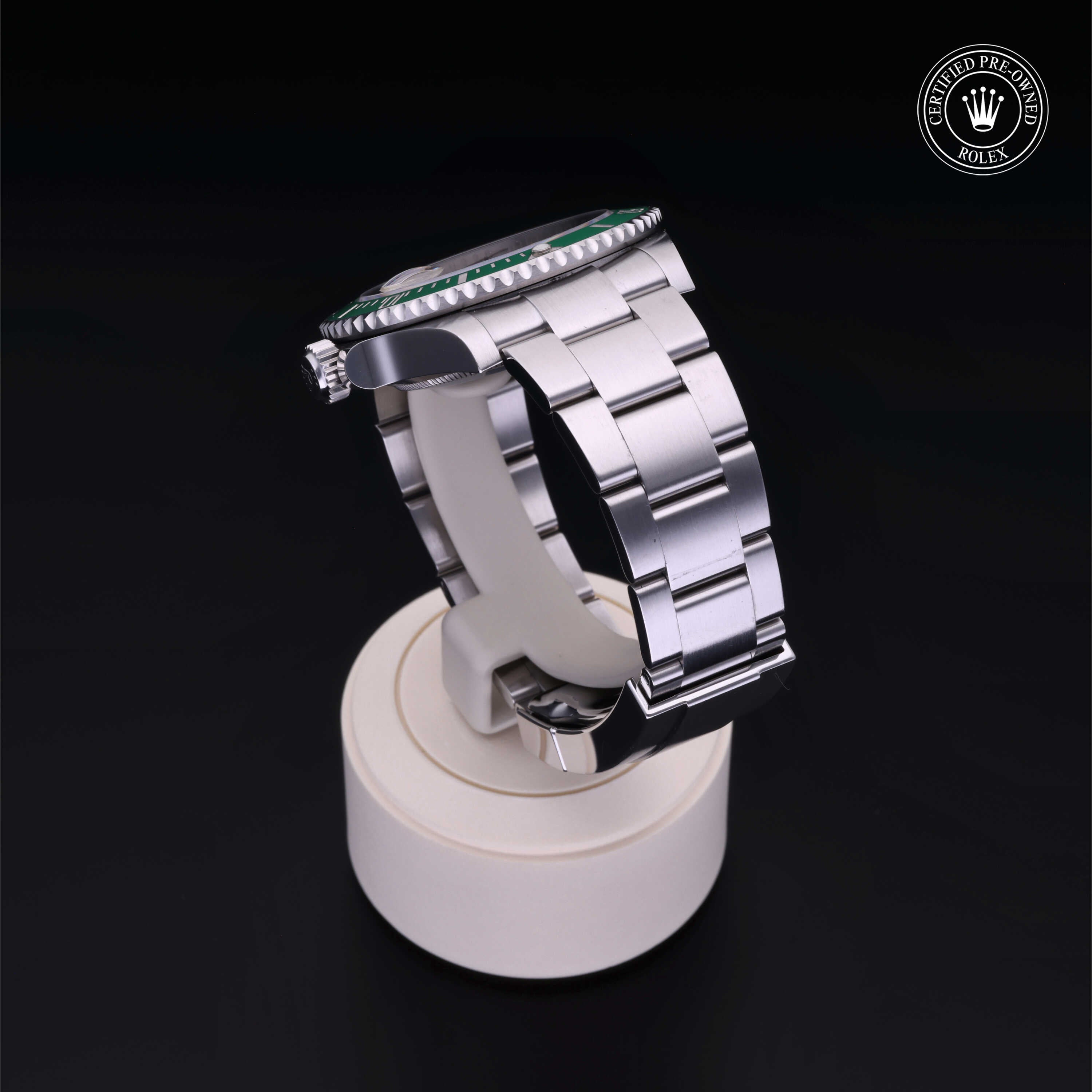 Side view of a luxury silver metal watch with a polished bracelet displayed on a beige stand against a black background, featuring a certified pre-owned Rolex emblem.