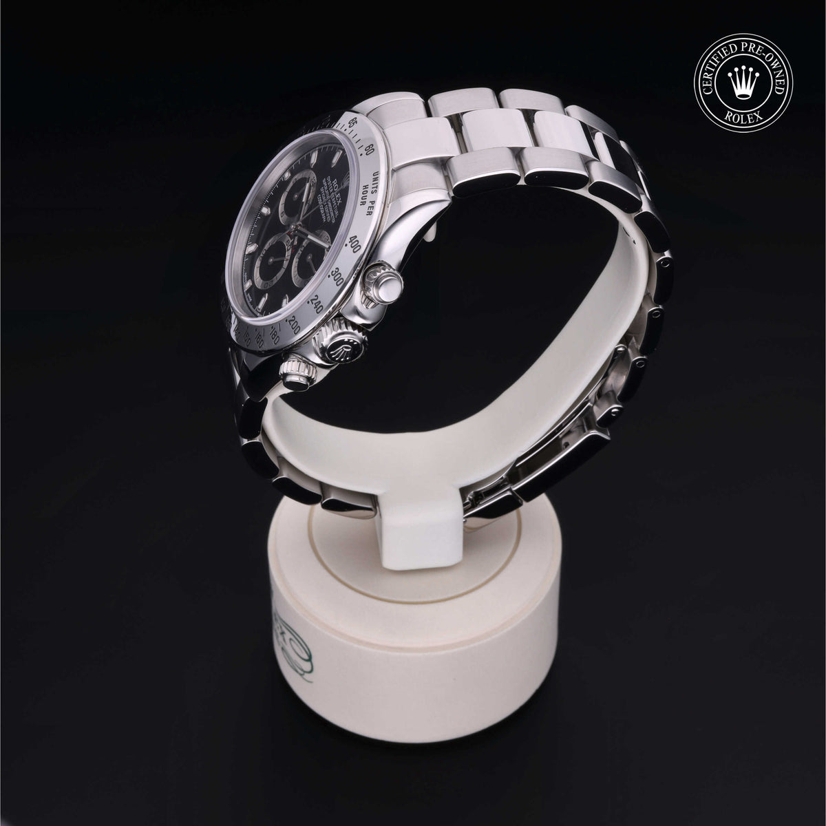 Silver Rolex chronograph watch with black dial displayed on a white stand against a black background, featuring the Certified Pre-Owned Rolex emblem.