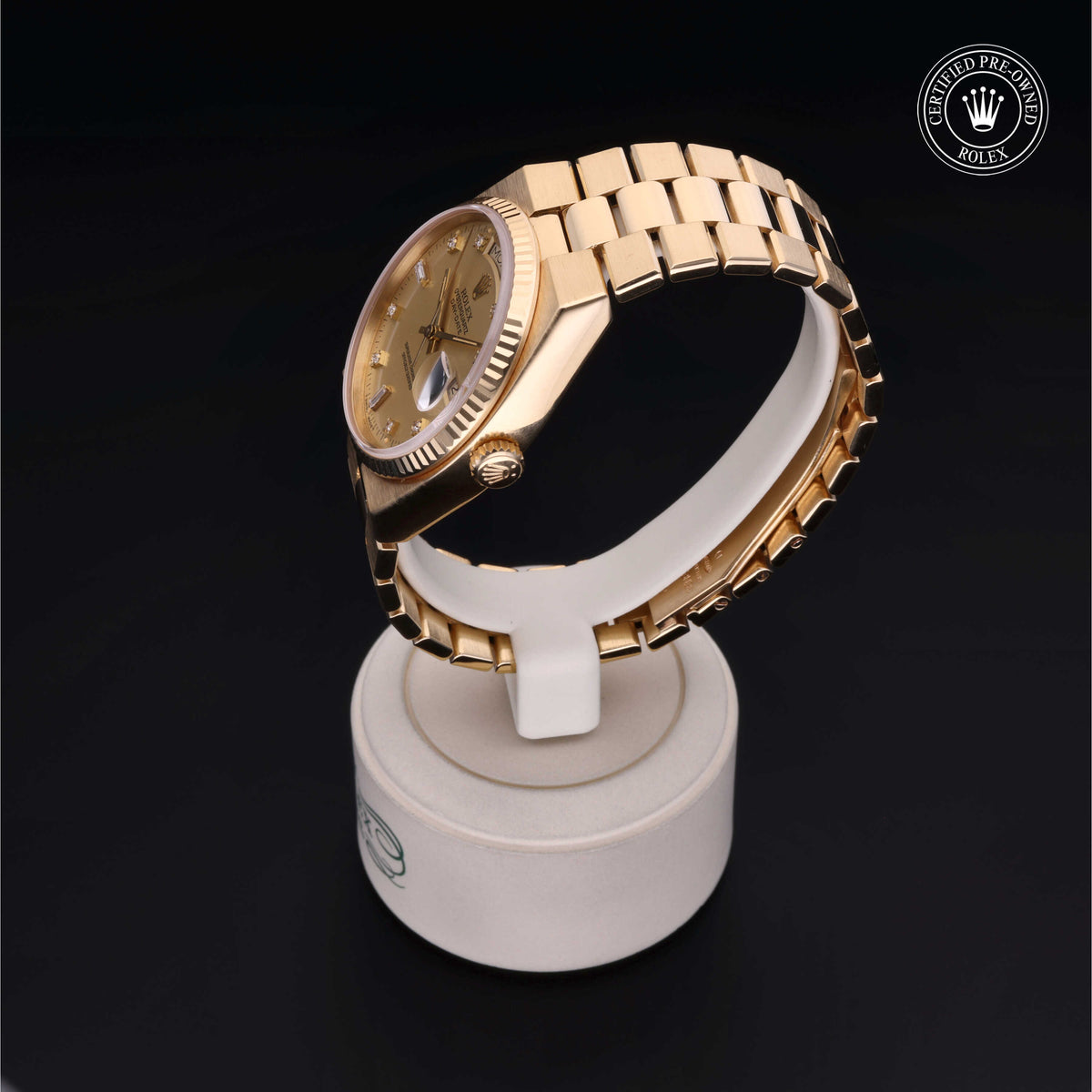 Gold Rolex luxury watch displayed on a white stand with a polished gold bracelet and fluted bezel, featuring a certified pre-owned Rolex emblem.