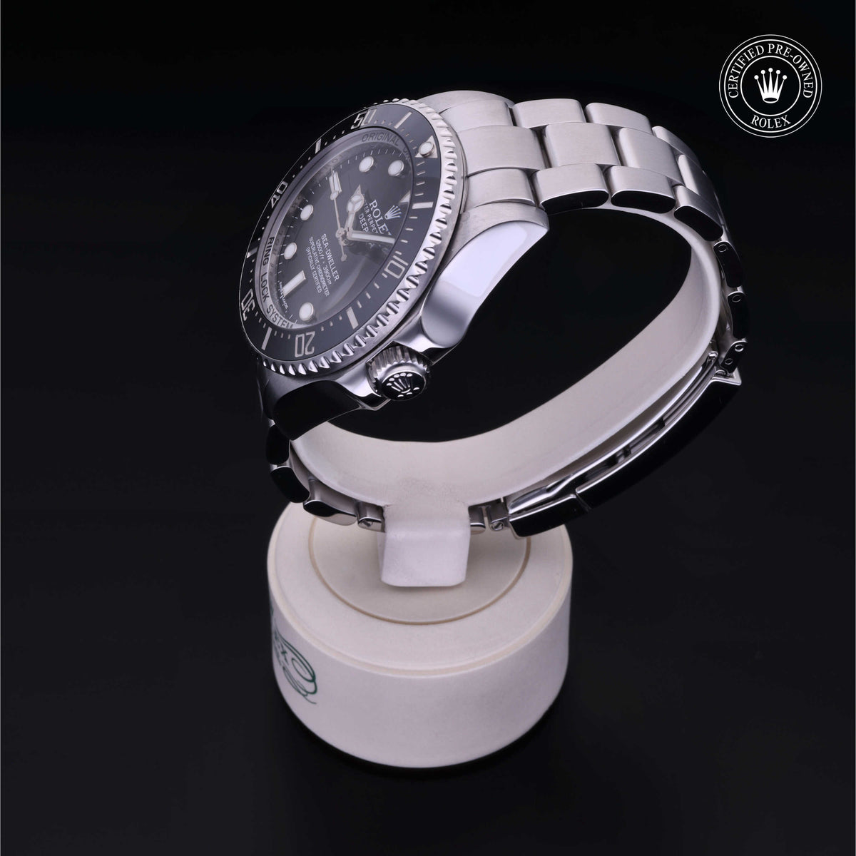Close-up of a Rolex luxury watch with a stainless steel band displayed on a white stand against a black background, featuring the Certified Pre-Owned Rolex badge.