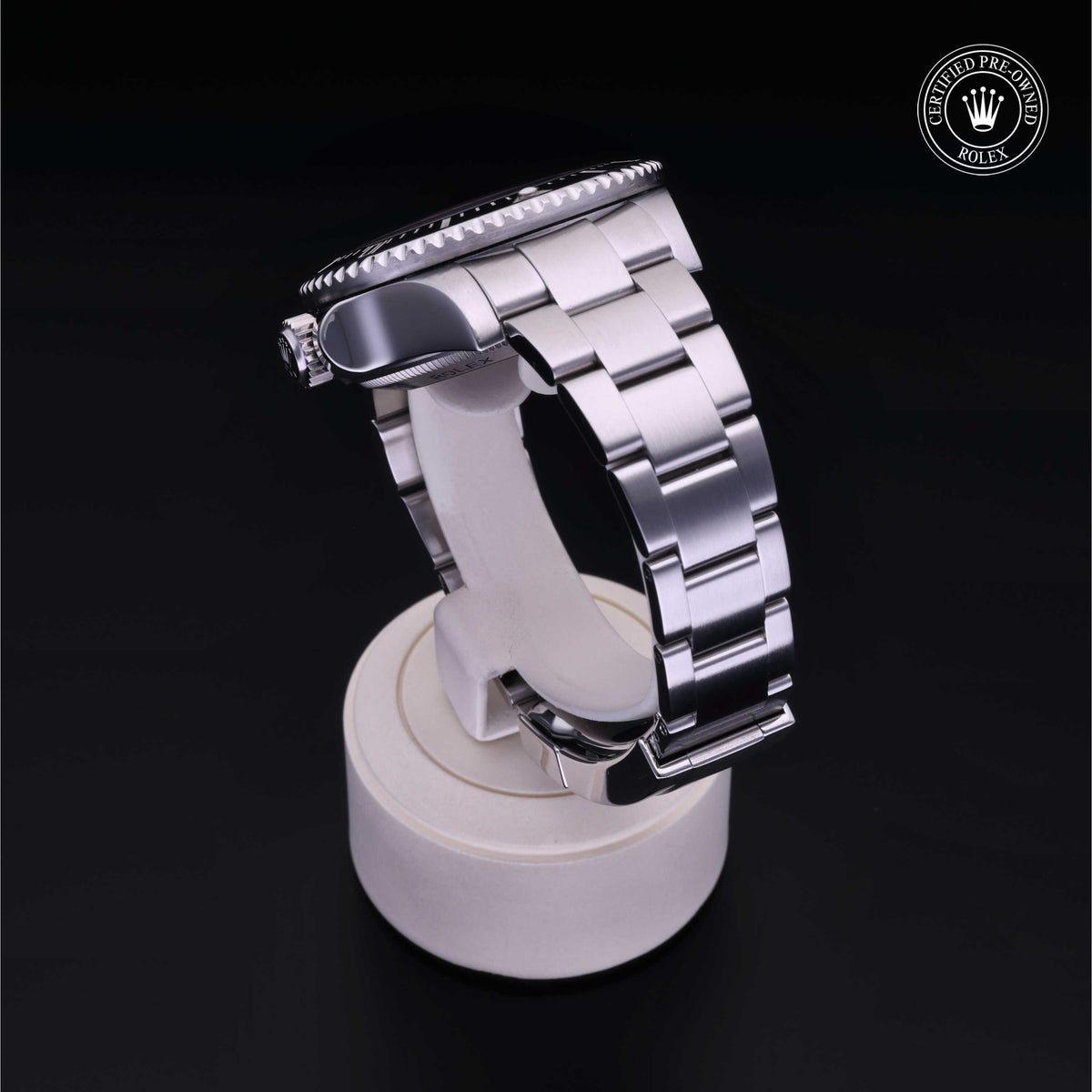 A close-up of a luxury stainless steel Rolex watch band displayed on a white stand, featuring a polished link bracelet and a 