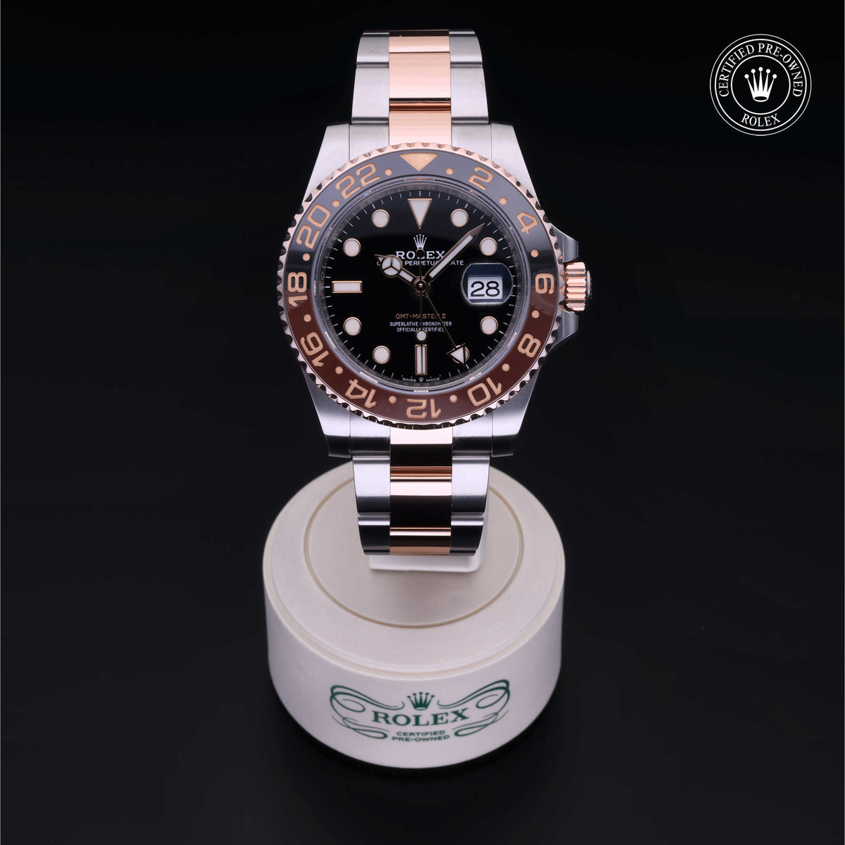 A two-tone Rolex watch with a black dial and rose gold accents, displayed on a branded stand with a Certified Pre-Owned Rolex logo on a black background.