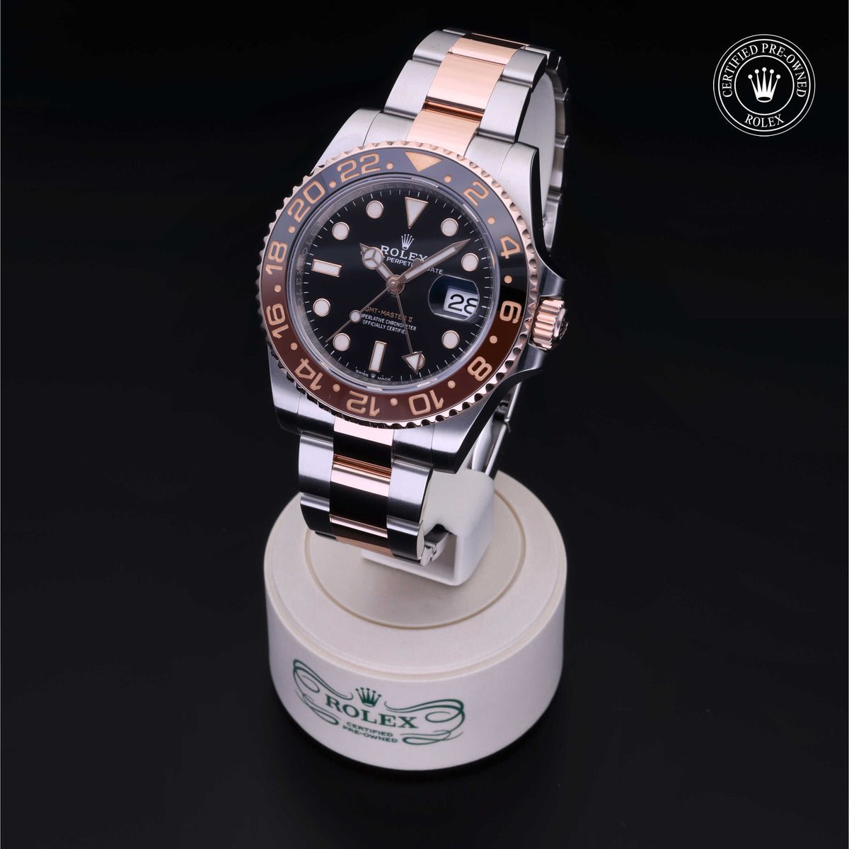 Rolex GMT-Master II with black and rose gold bezel, stainless steel and rose gold bracelet, displayed on a white stand with Rolex branding and a certified pre-owned logo.