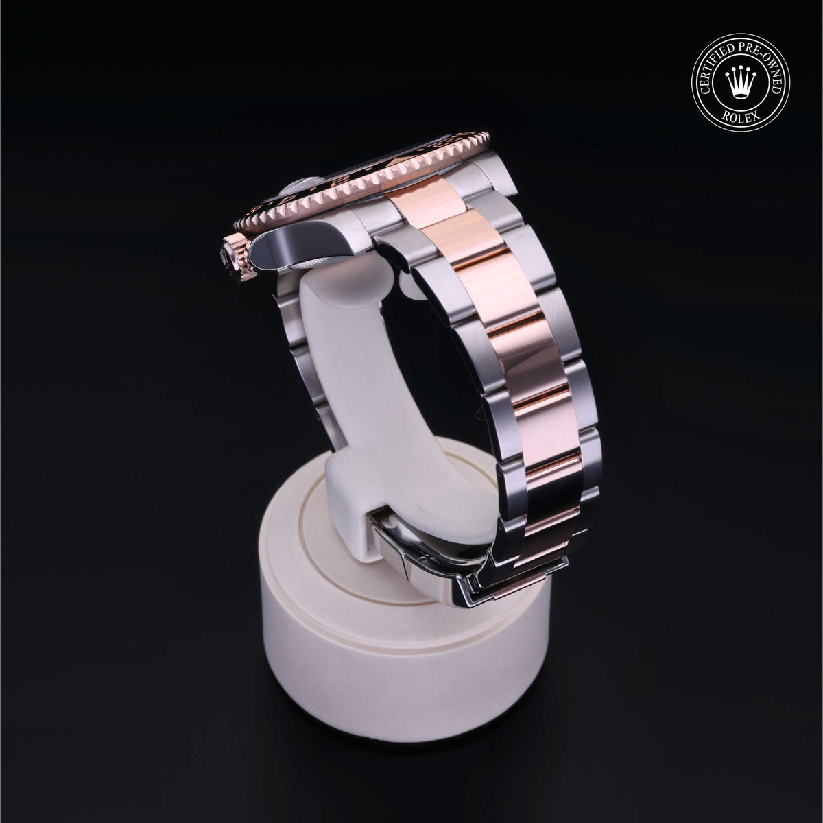 Close-up of a two-tone luxury watch bracelet with polished silver and rose gold links displayed on a white stand, featuring a certified pre-owned Rolex logo.