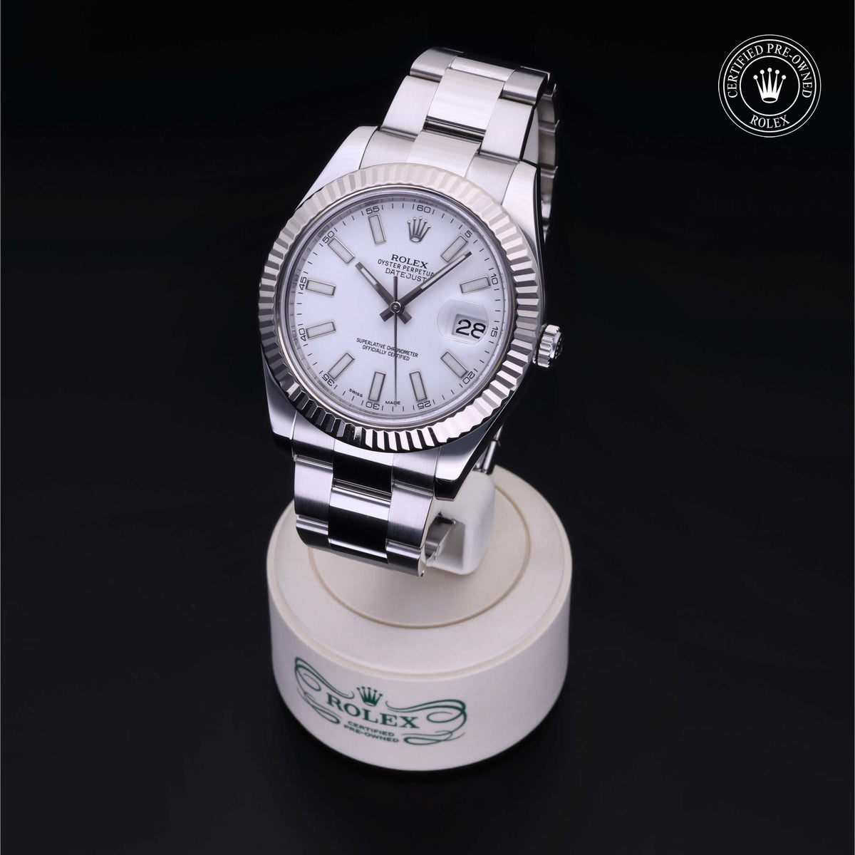 A close-up of a Rolex luxury watch with a silver metal band and white face, displayed on a branded stand with a 