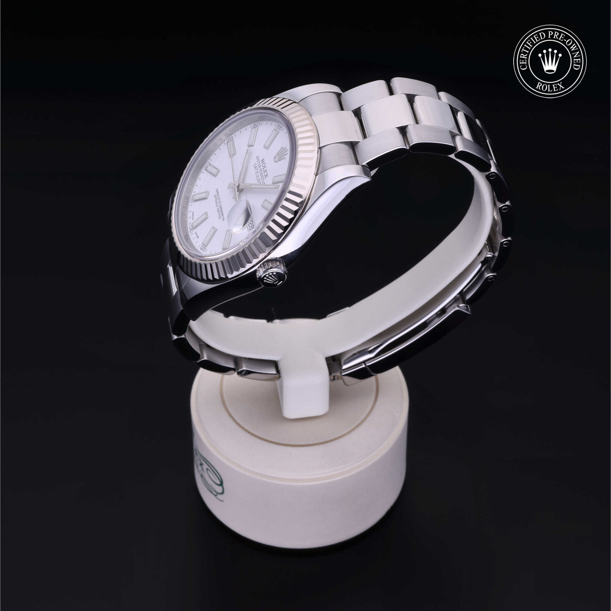 Silver Rolex wristwatch with a white dial and fluted bezel displayed on a white stand against a black background, featuring a certified pre-owned Rolex logo.