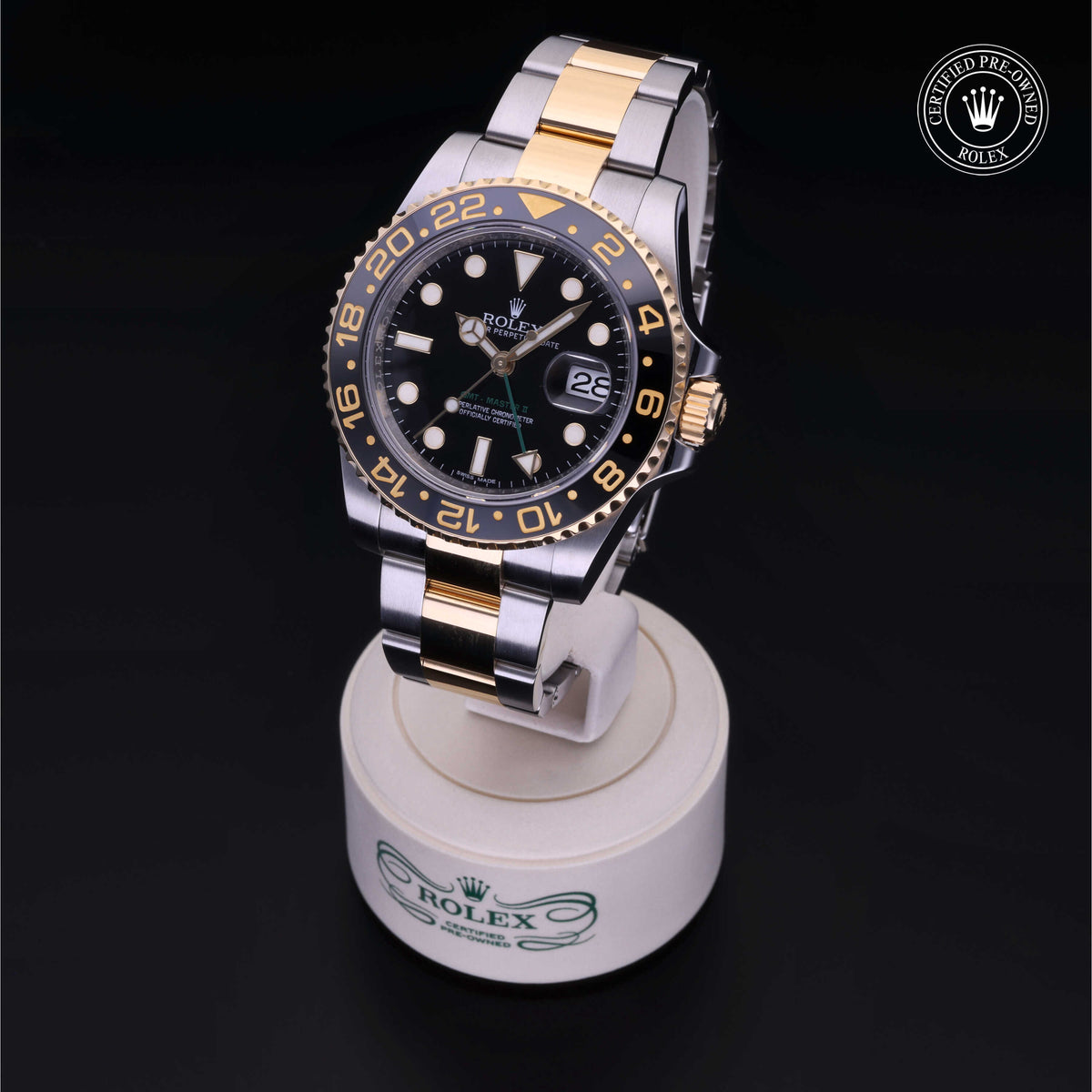 Two-tone Rolex watch with black dial and gold accents displayed on a branded watch stand, featuring Rolex Certified Pre-Owned logo in the corner.