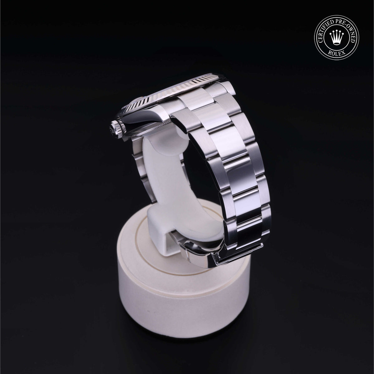 Close-up of a polished stainless steel Rolex watch with a metal link bracelet displayed on a white stand against a black background, showcasing luxury watch craftsmanship.