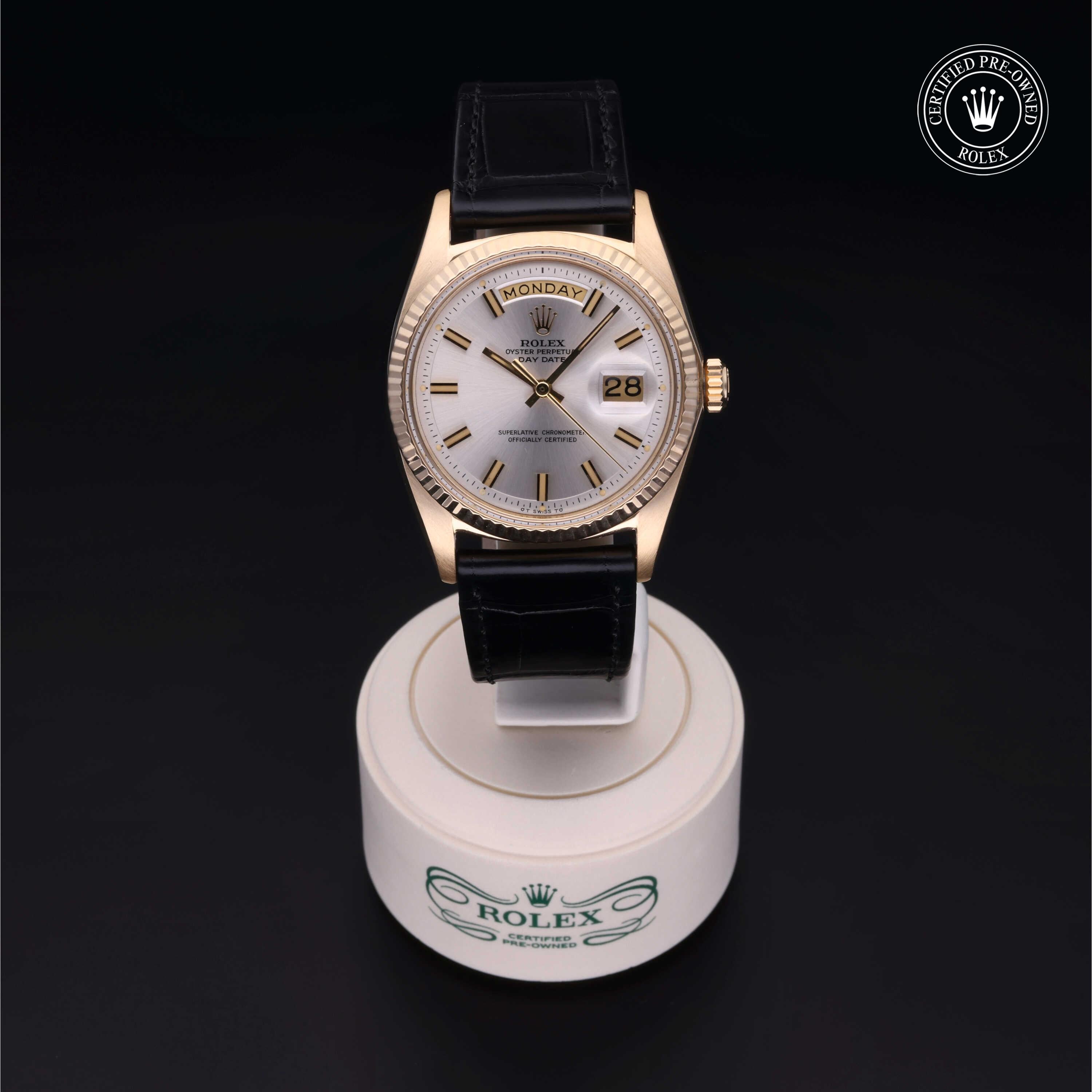 Luxury Rolex watch with gold bezel and black leather strap displayed on a white branded stand, showcasing the day and date feature under elegant lighting.