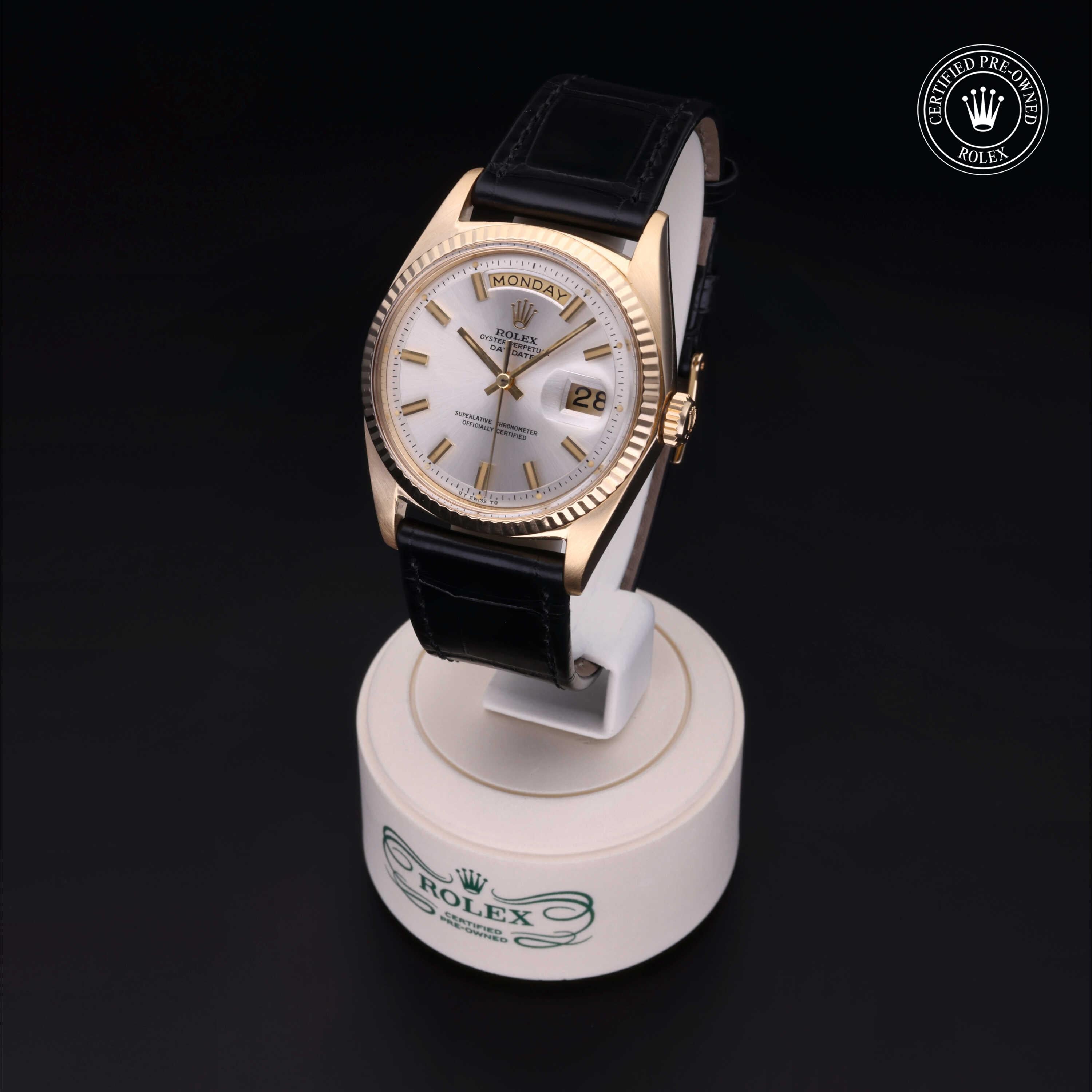 Rolex luxury watch with gold case, white dial, day and date display, black leather strap, displayed on a round stand with Rolex branding and certified pre-owned logo.
