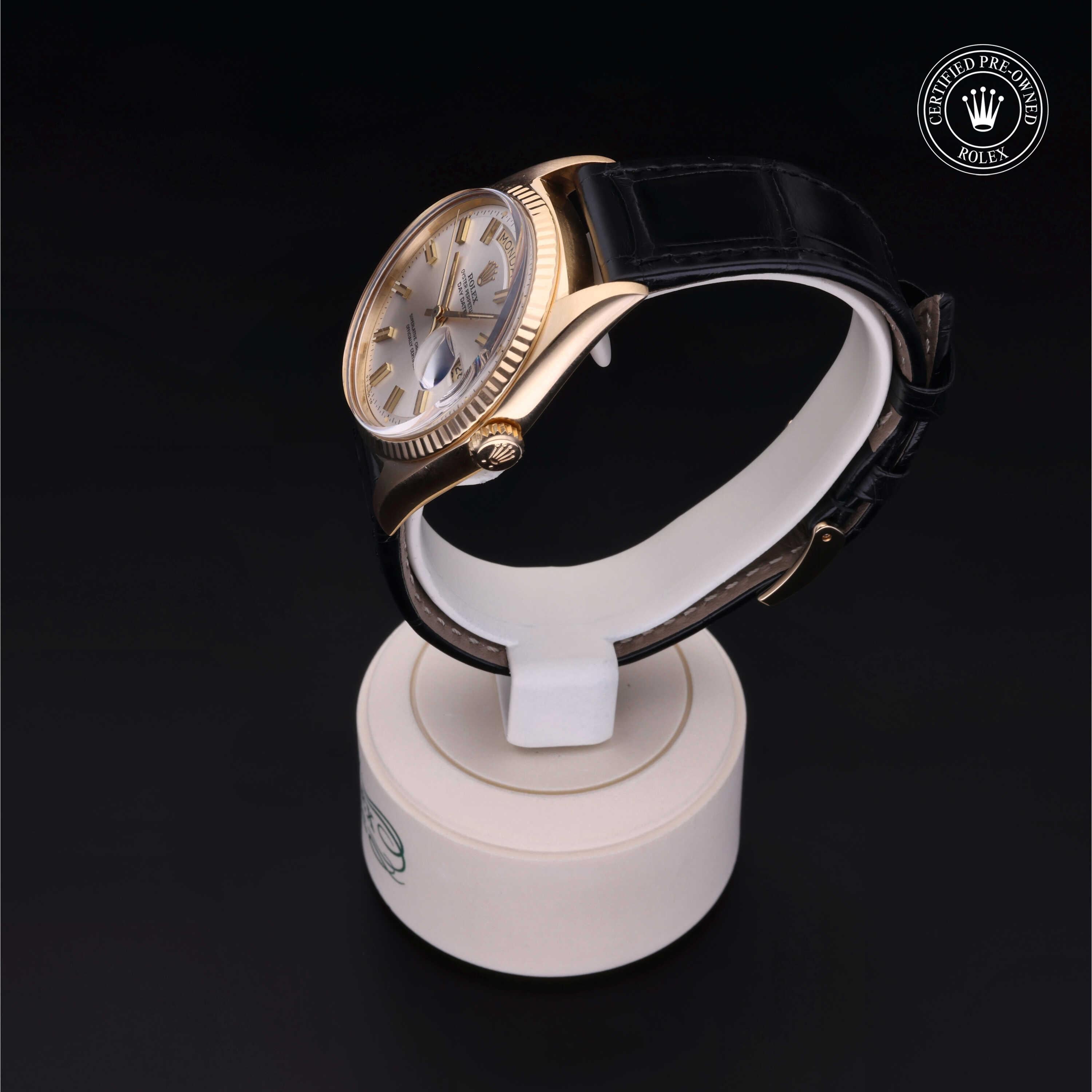 Gold Rolex wristwatch with a black leather strap displayed on a white stand against a dark background, featuring the Rolex Certified Pre-Owned logo.