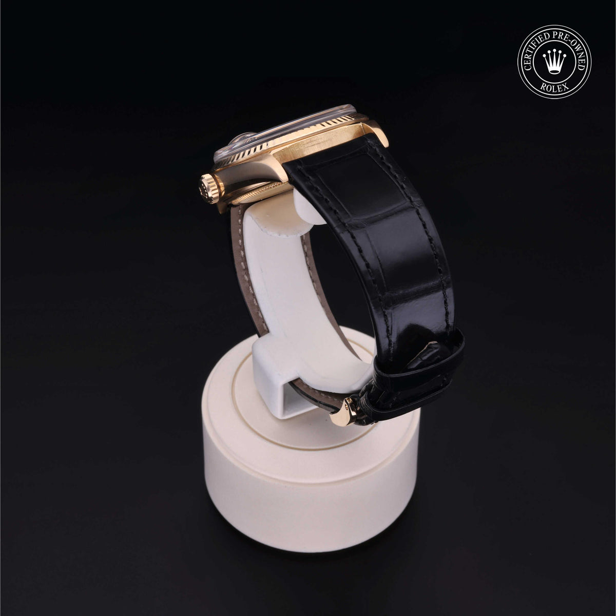 Side view of a Rolex luxury watch with a black leather strap displayed on a white stand against a black background, featuring the Rolex Certified Pre-Owned logo.