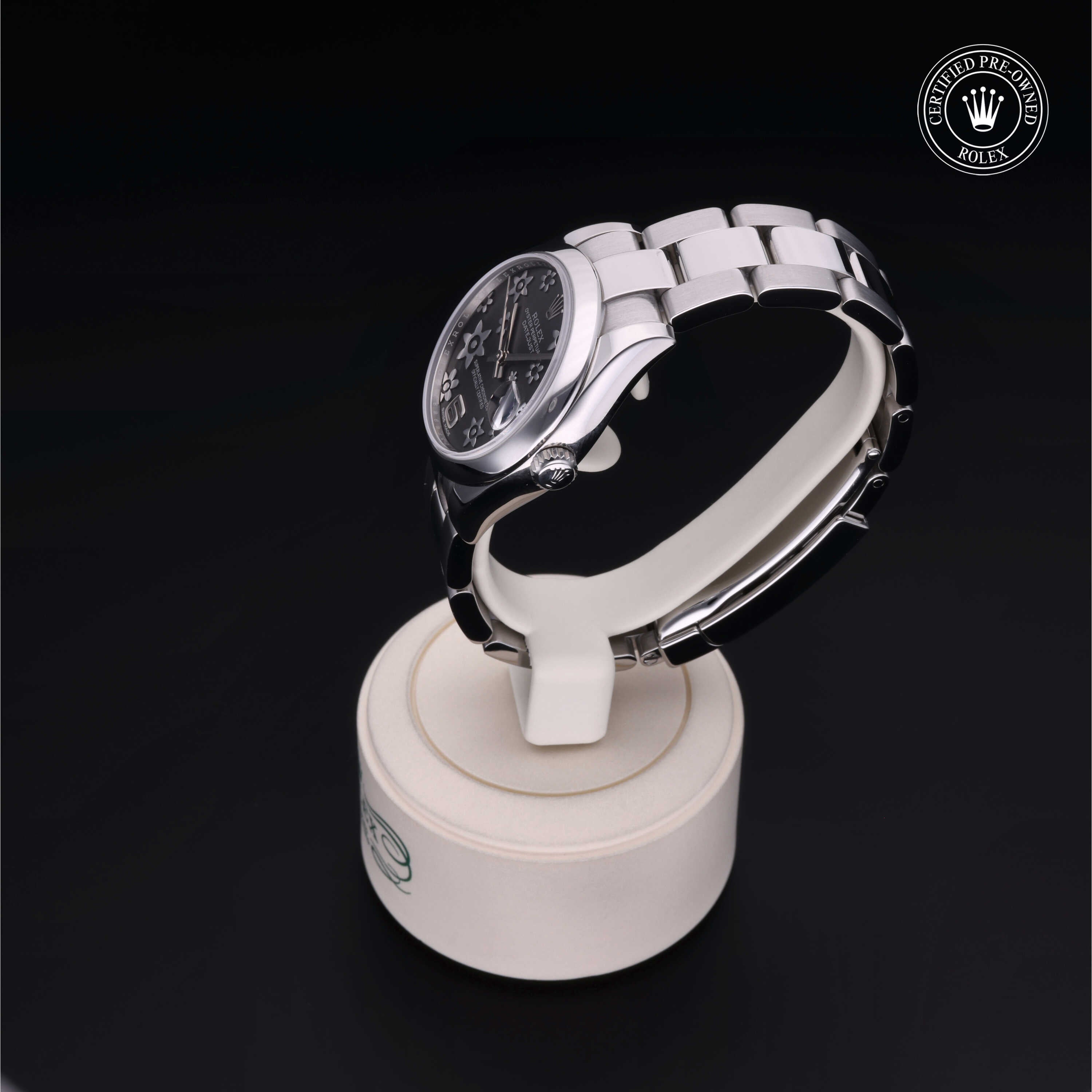 Silver Rolex luxury watch with a black dial displayed on a white stand, featuring a metal link bracelet and a certified pre-owned Rolex logo on a dark background.