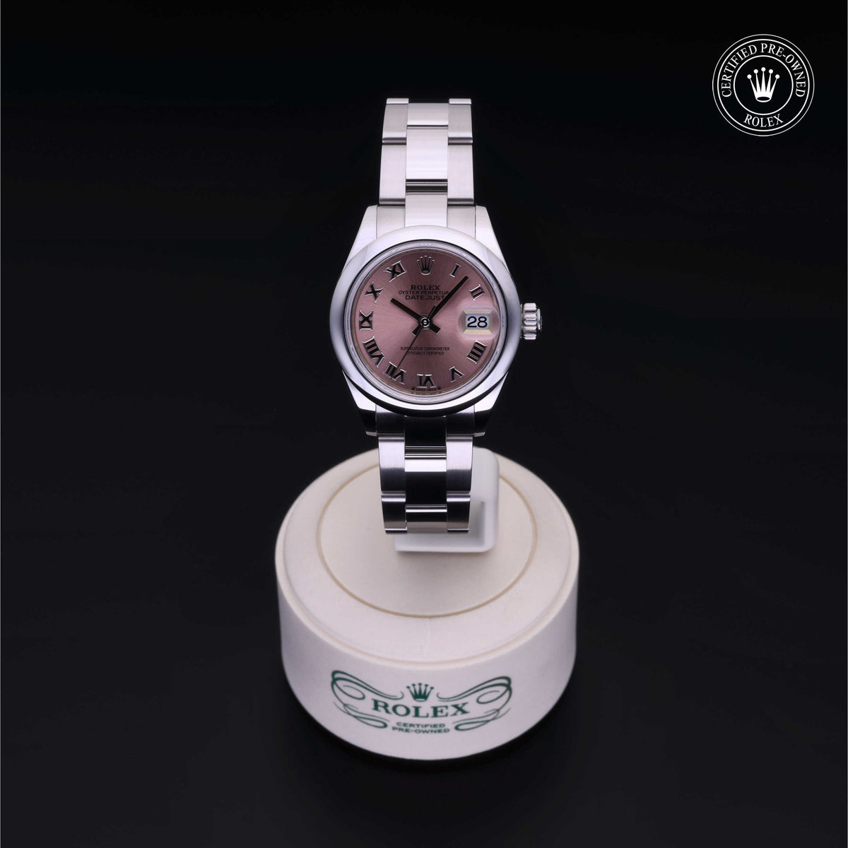 Rolex luxury watch with a stainless steel bracelet and rose-colored dial featuring Roman numerals, displayed on a branded stand with a Certified Pre-Owned Rolex logo.