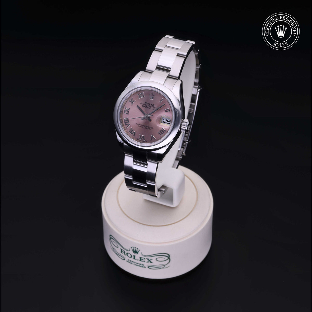 Stainless steel Rolex watch with a pink dial and Roman numeral markers displayed on a branded stand, highlighting luxury and precision craftsmanship.