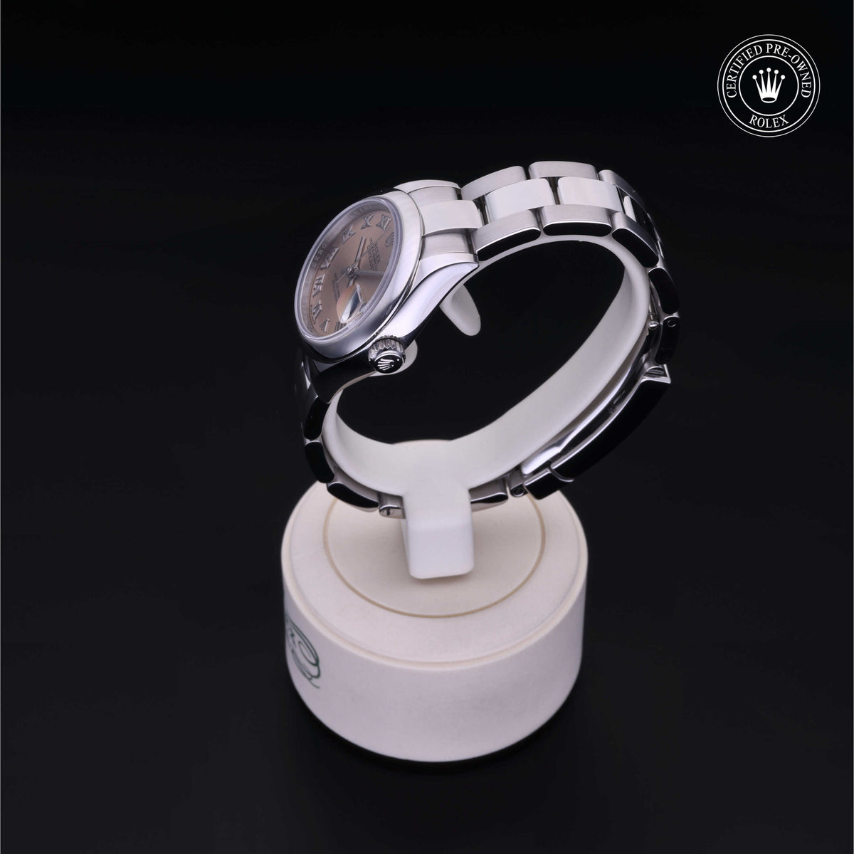 Silver Rolex watch with a metal bracelet displayed on a white stand against a black background, featuring a certified pre-owned Rolex logo in the corner.