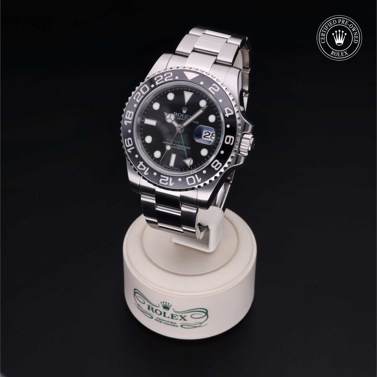 Rolex luxury watch with black dial and silver metal bracelet displayed on a white Rolex stand, featuring a certified pre-owned Rolex logo in the corner.
