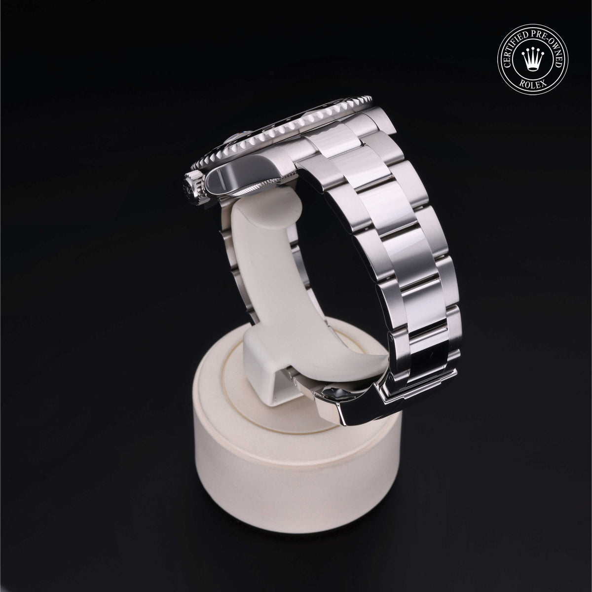 Side view of a polished stainless steel Rolex watch with a metal link bracelet displayed on a light-colored stand against a black background, certified pre-owned.