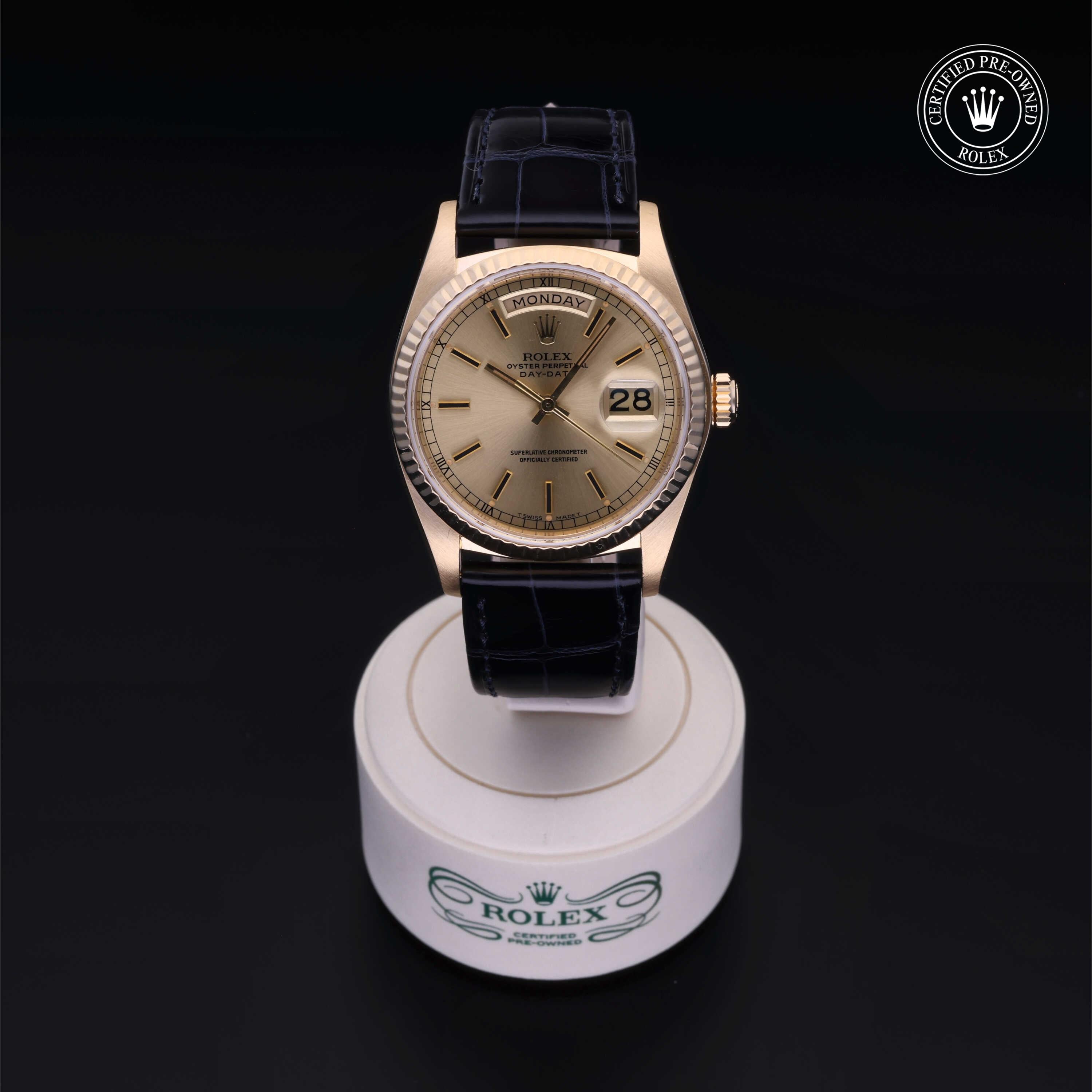 Gold Rolex wristwatch with black leather strap displayed on a white circular stand, featuring a day and date function and a certified pre-owned Rolex logo in the corner.