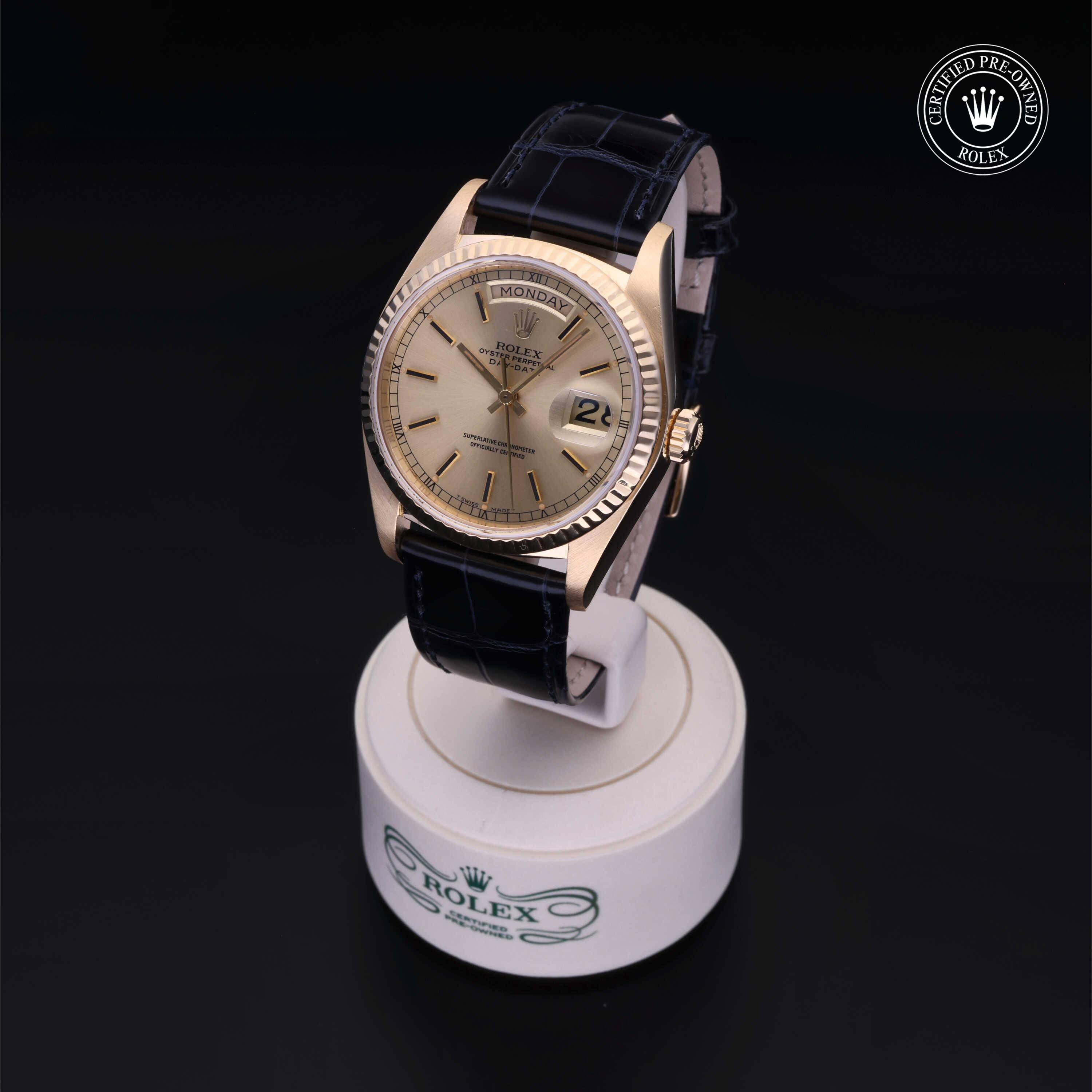 Gold Rolex watch with a black leather strap displayed on a white stand featuring the Rolex logo, marked as certified pre-owned, highlighting fine luxury timepieces.