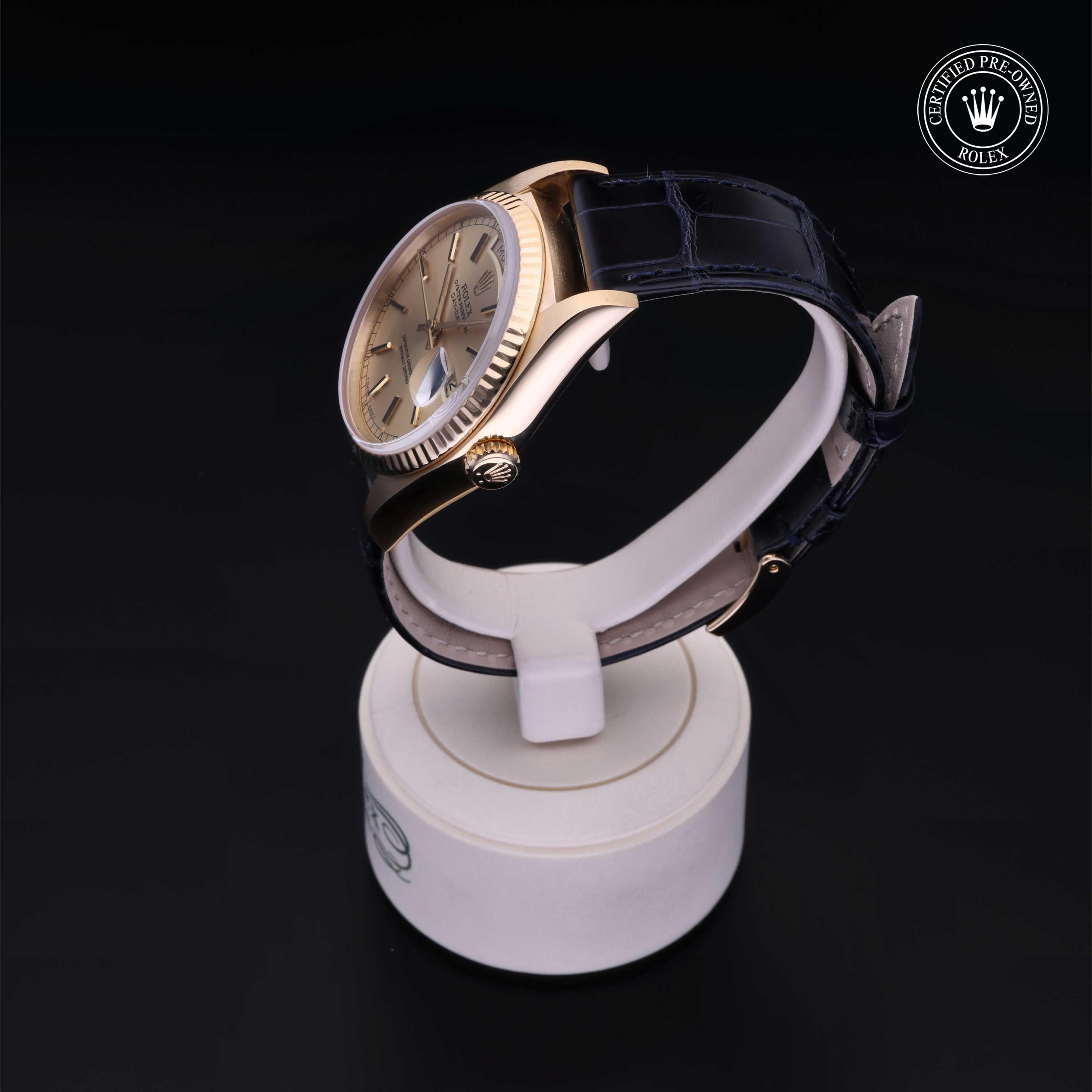 Side view of a luxury Rolex watch with a gold bezel and black leather strap displayed on a white stand against a black background, highlighting fine craftsmanship.