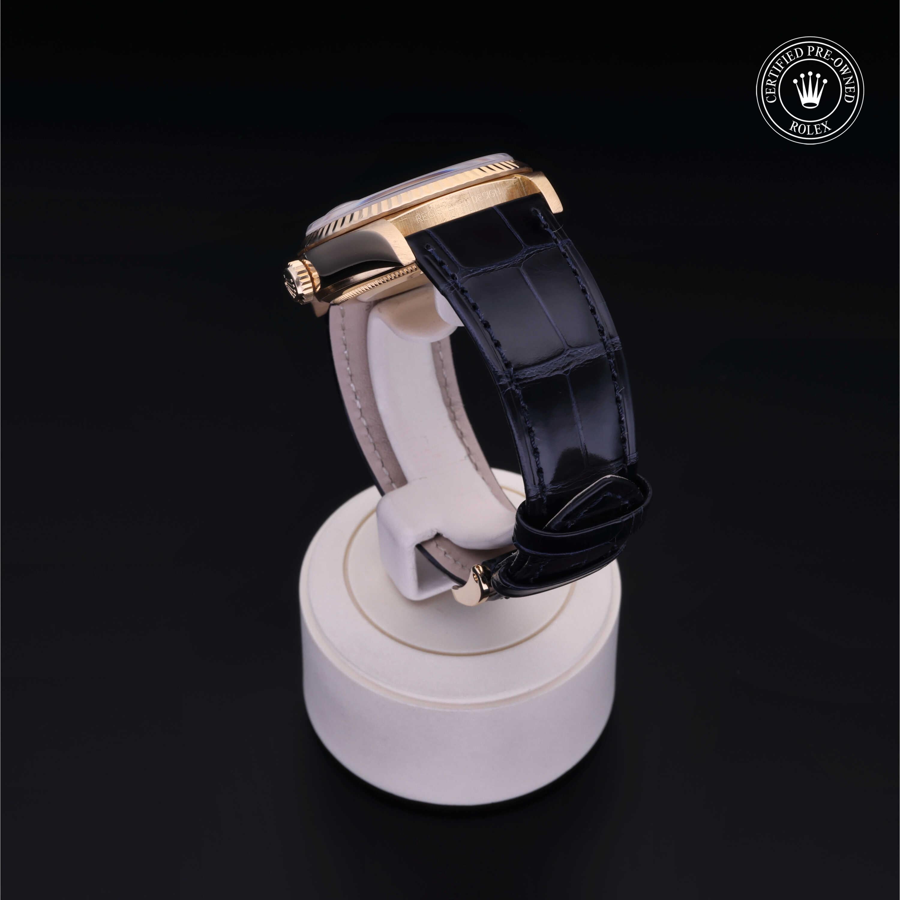 Side view of a Rolex Certified Pre-Owned luxury watch with a gold case and black leather strap displayed on a white stand against a black background.