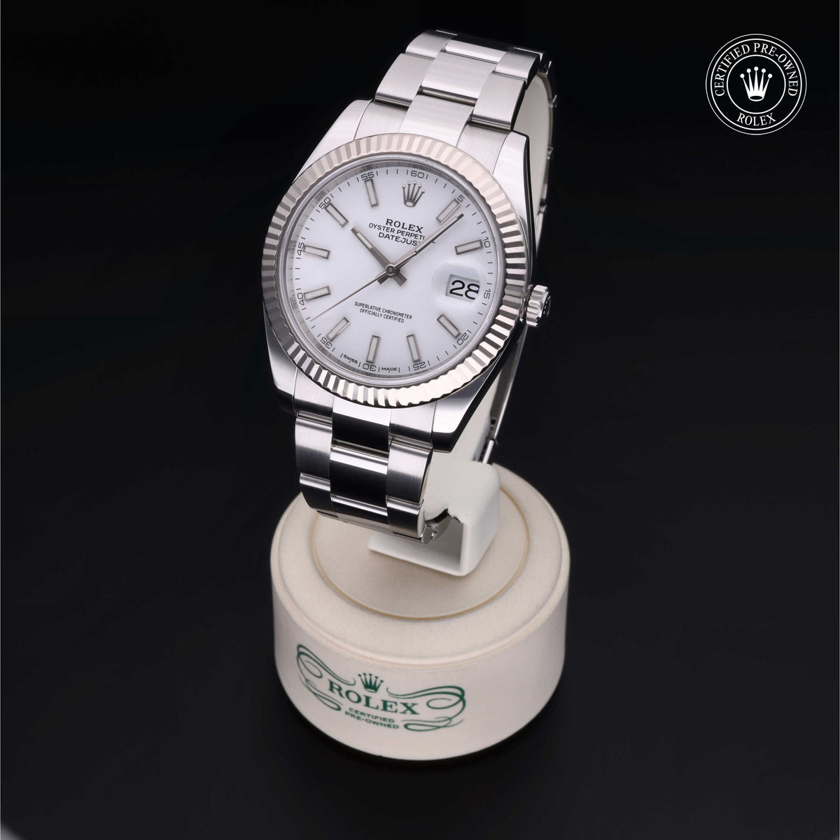 Rolex Datejust luxury watch with silver bracelet and white dial featuring date display, shown on a branded stand with certified pre-owned Rolex emblem in the background.