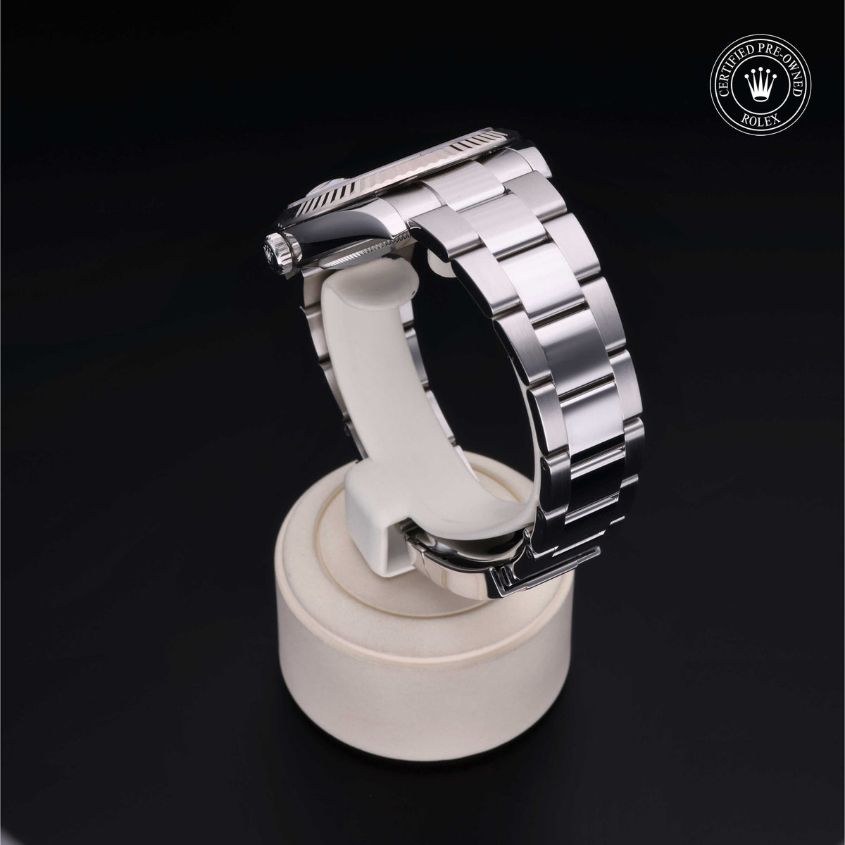 Close-up of a polished silver luxury watch band displayed on a white stand with a black background and a certified pre-owned Rolex emblem in the corner.