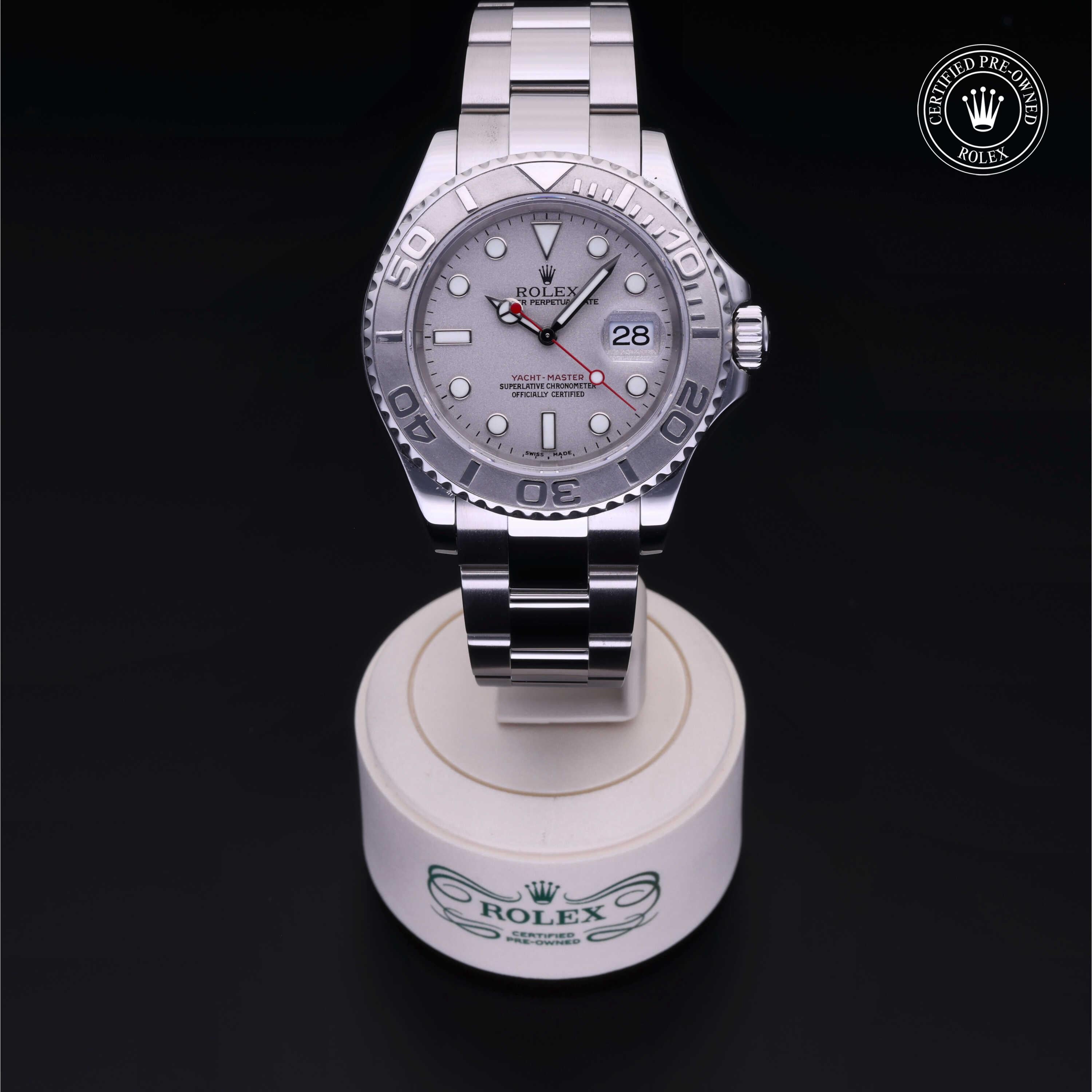 Silver Rolex Yacht-Master watch with a metal bracelet displayed on a white stand, featuring a date window and a red second hand, against a black background with a Rolex Certified Pre-Owned badge.