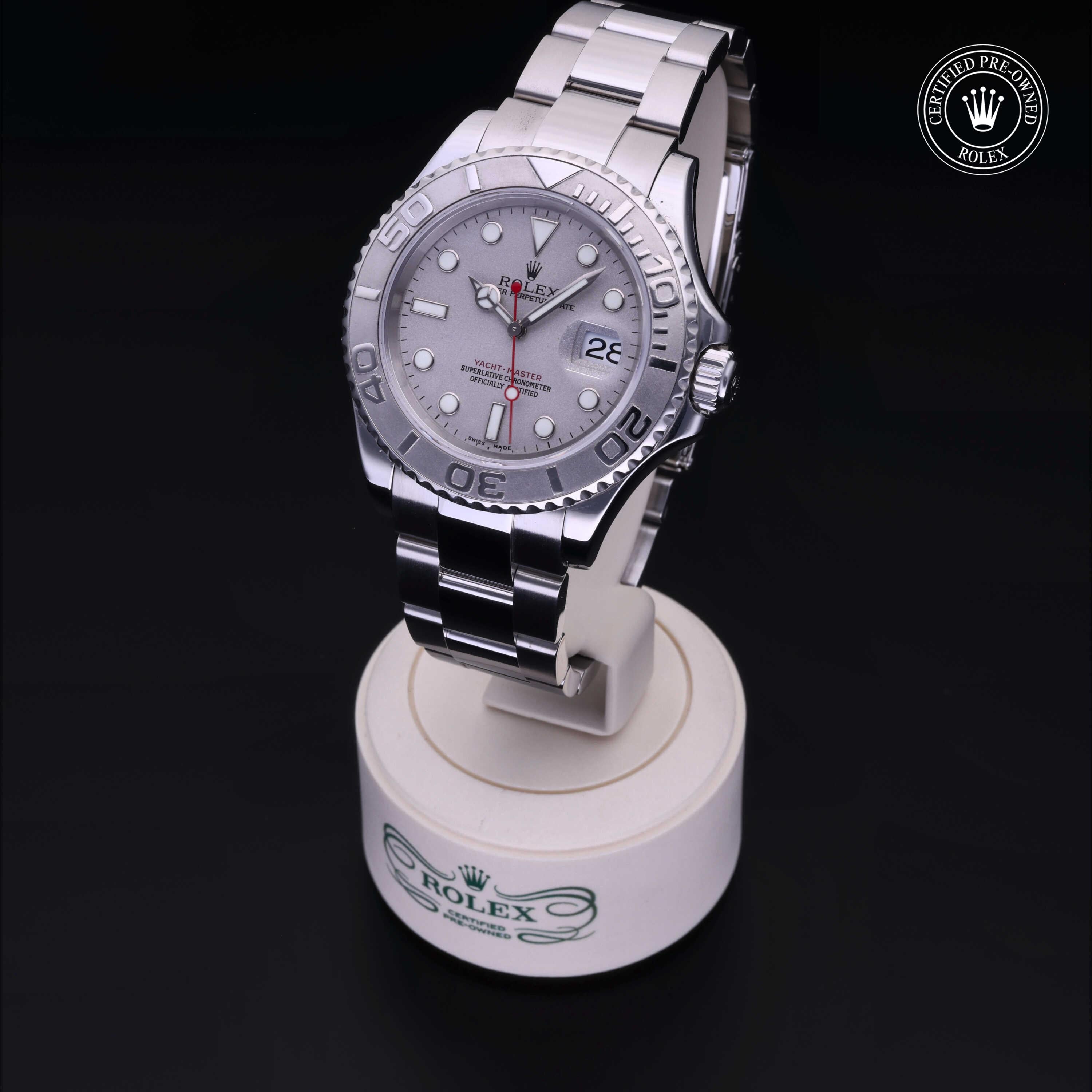 Silver Rolex luxury watch with a stainless steel bracelet displayed on a white stand, featuring a date window and certified pre-owned Rolex emblem.