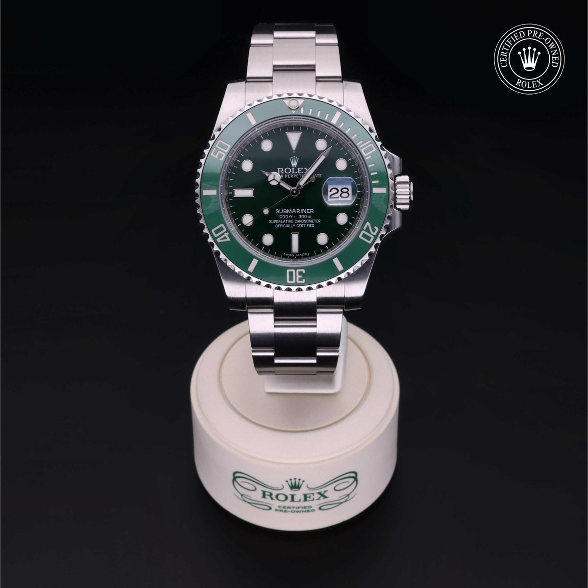 Rolex Submariner wristwatch with green bezel and stainless steel bracelet displayed on a branded stand, featuring a certified pre-owned Rolex logo in the corner.