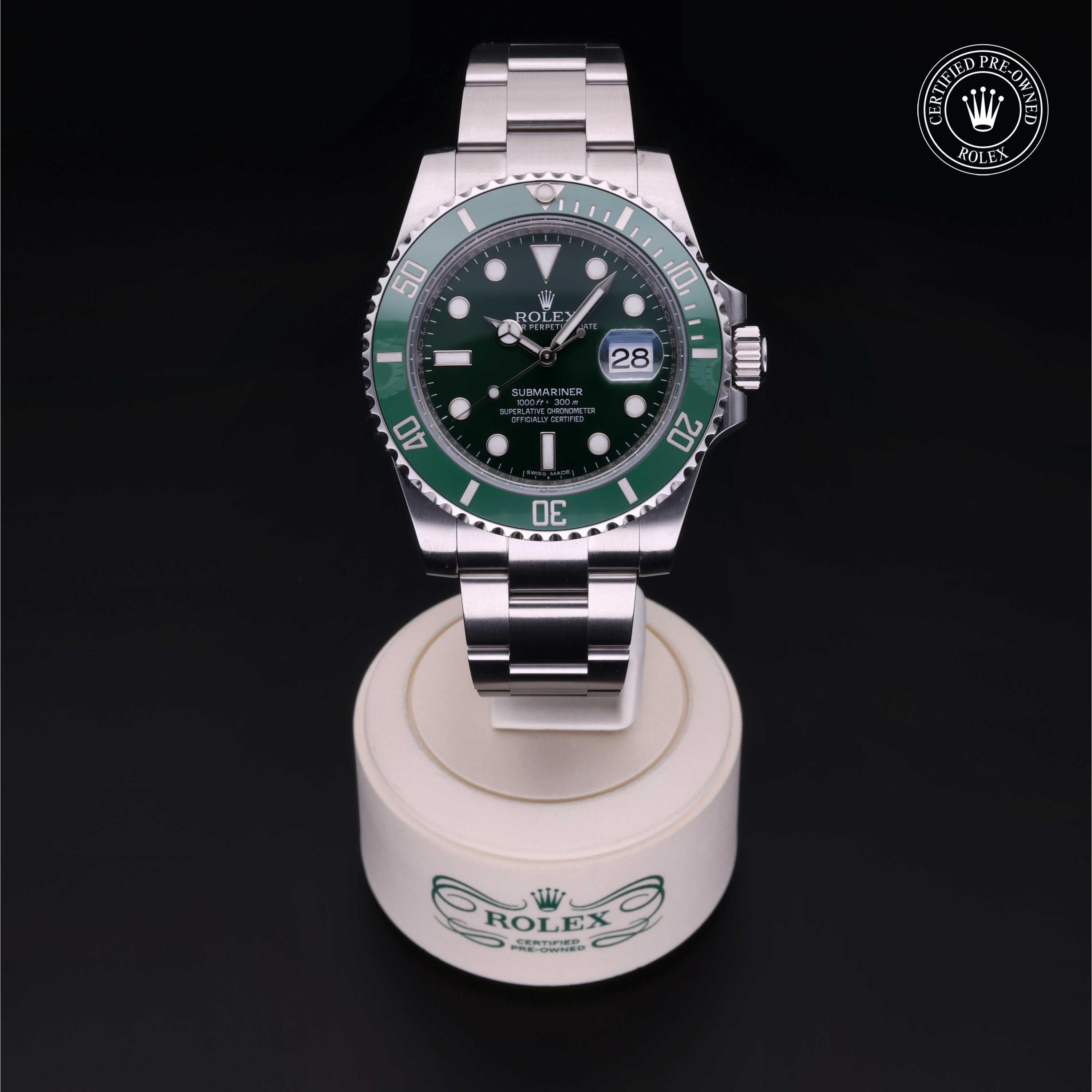 Rolex Submariner wristwatch with green bezel and stainless steel bracelet displayed on a branded stand, featuring a certified pre-owned Rolex logo in the corner.