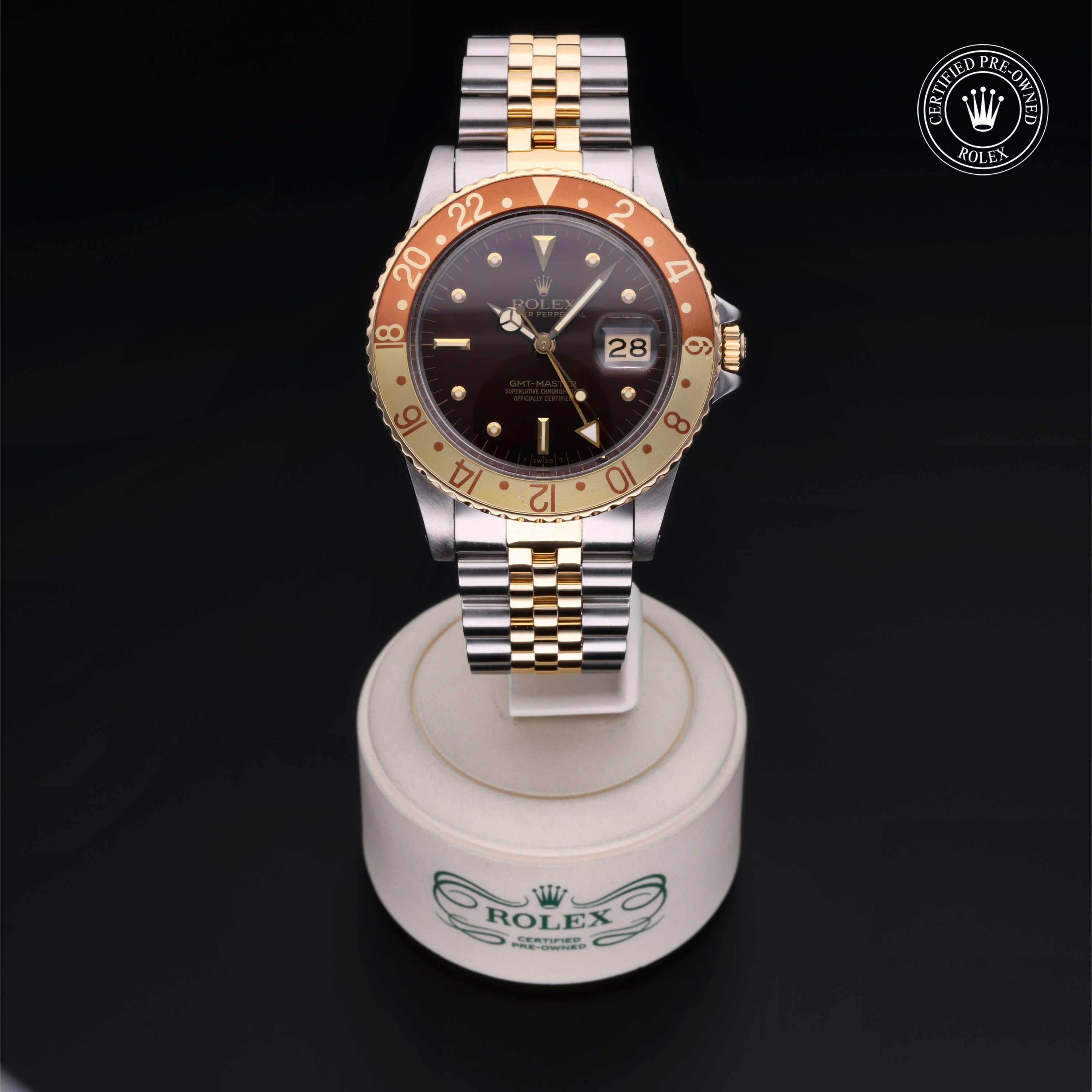 Two-tone Rolex wristwatch with a brown and gold bezel, black dial, date display, and Jubilee bracelet displayed on a round white stand with Rolex branding against a black background.