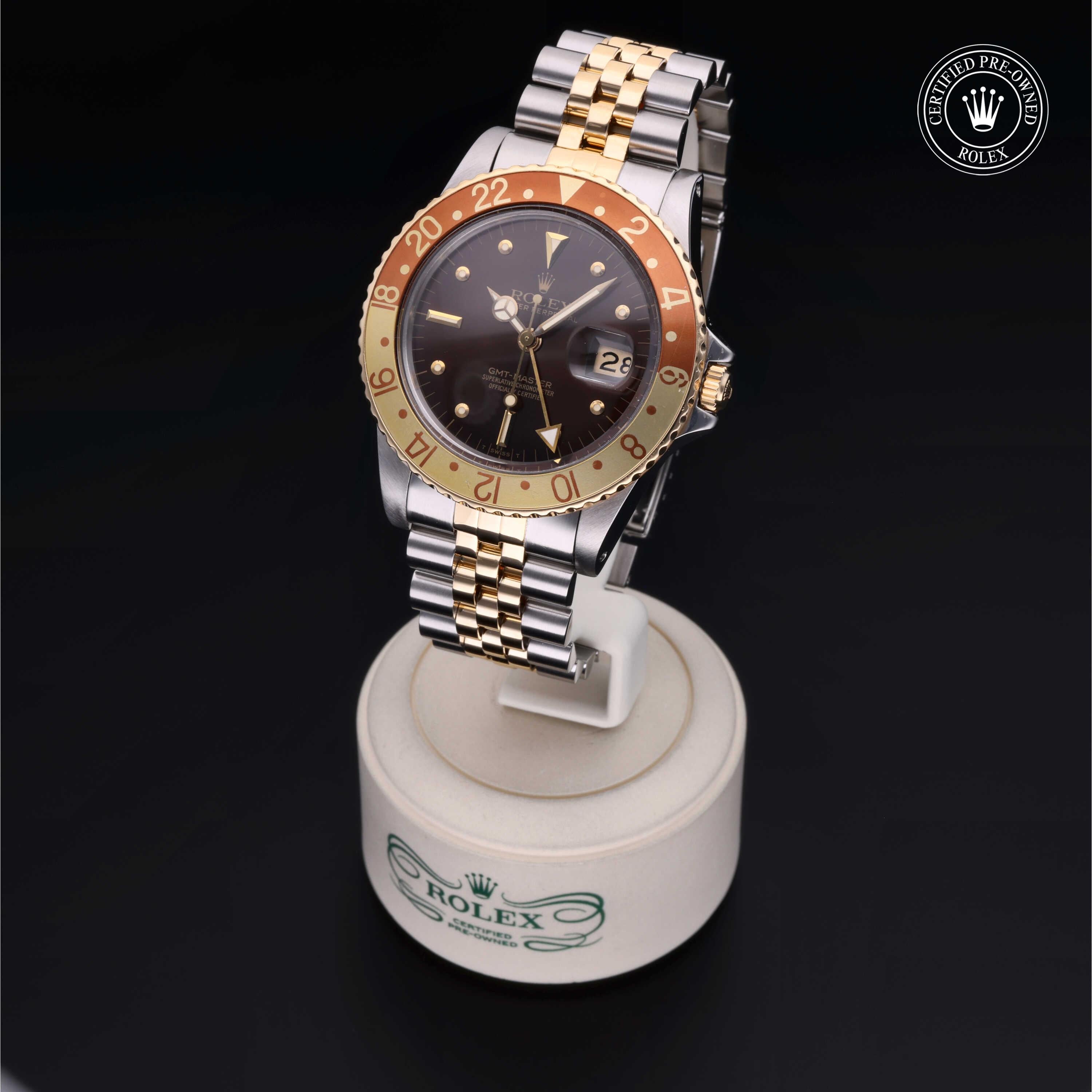 Rolex luxury watch with two-tone gold and silver bracelet, black dial, and brown bezel, displayed on a branded stand with a certified pre-owned logo.