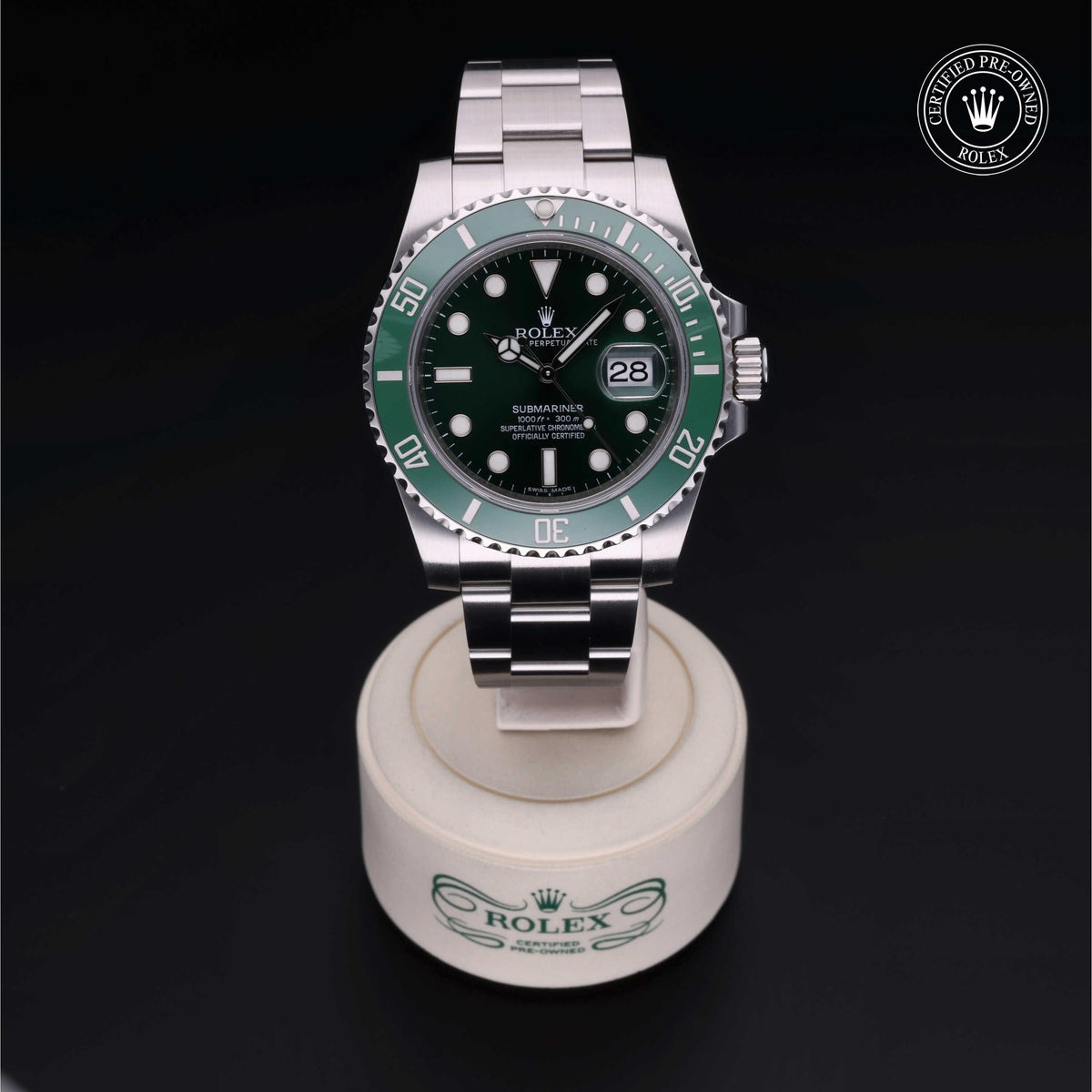 Rolex Submariner watch with a green bezel and black dial displayed on a branded stand against a black background, highlighting luxury timepiece craftsmanship.