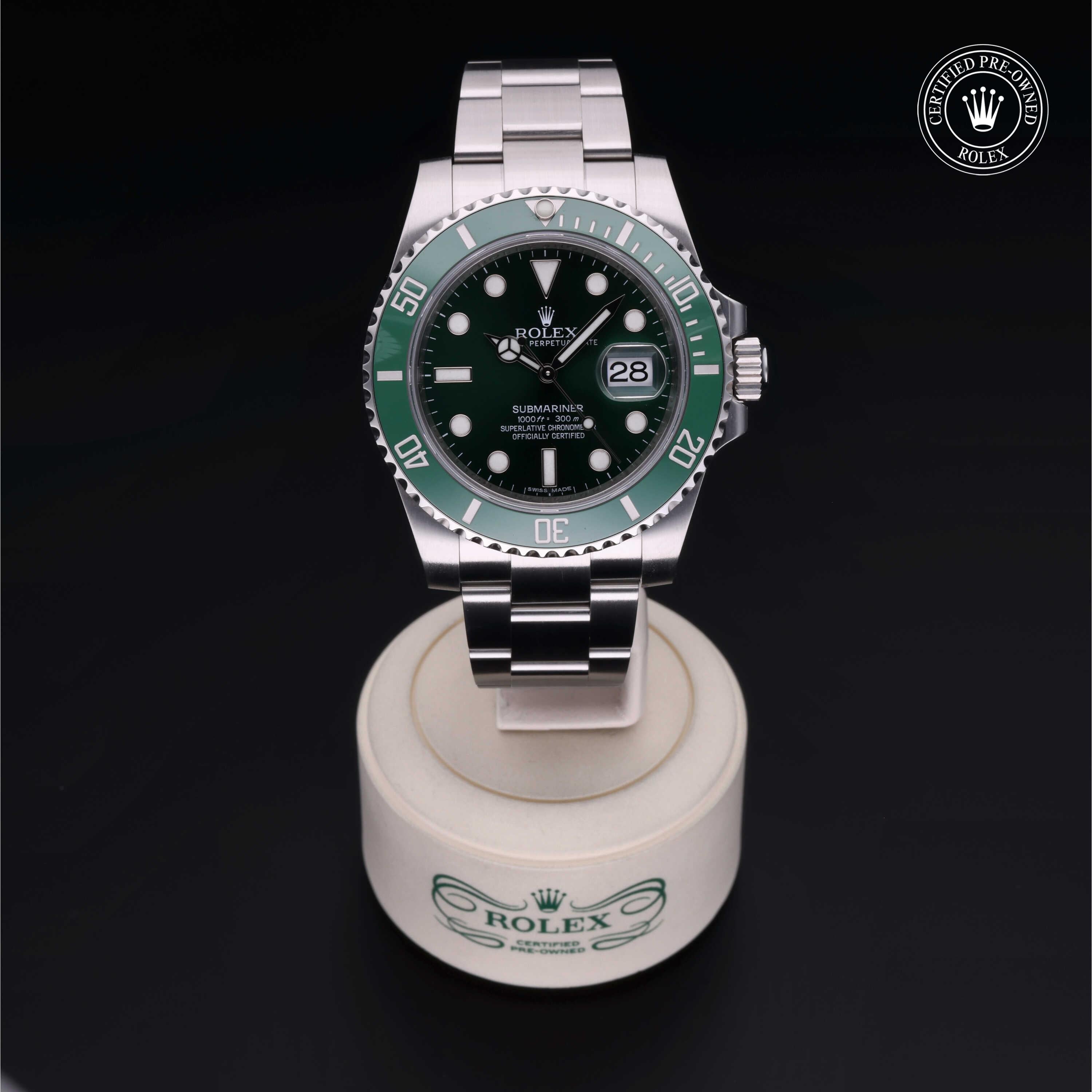 Rolex Submariner watch with a green bezel and black dial displayed on a branded stand against a black background, highlighting luxury timepiece craftsmanship.