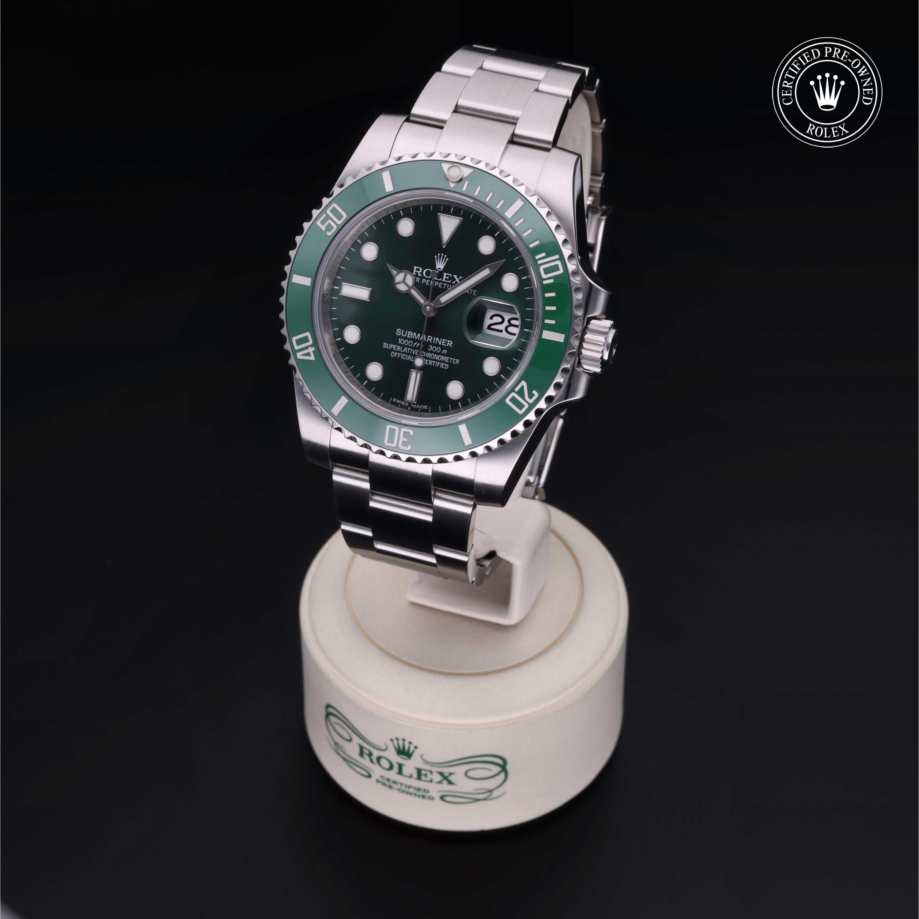 A Rolex Submariner luxury watch with a green bezel and stainless steel bracelet, displayed on a branded stand with a Certified Pre-Owned Rolex logo on a dark background.