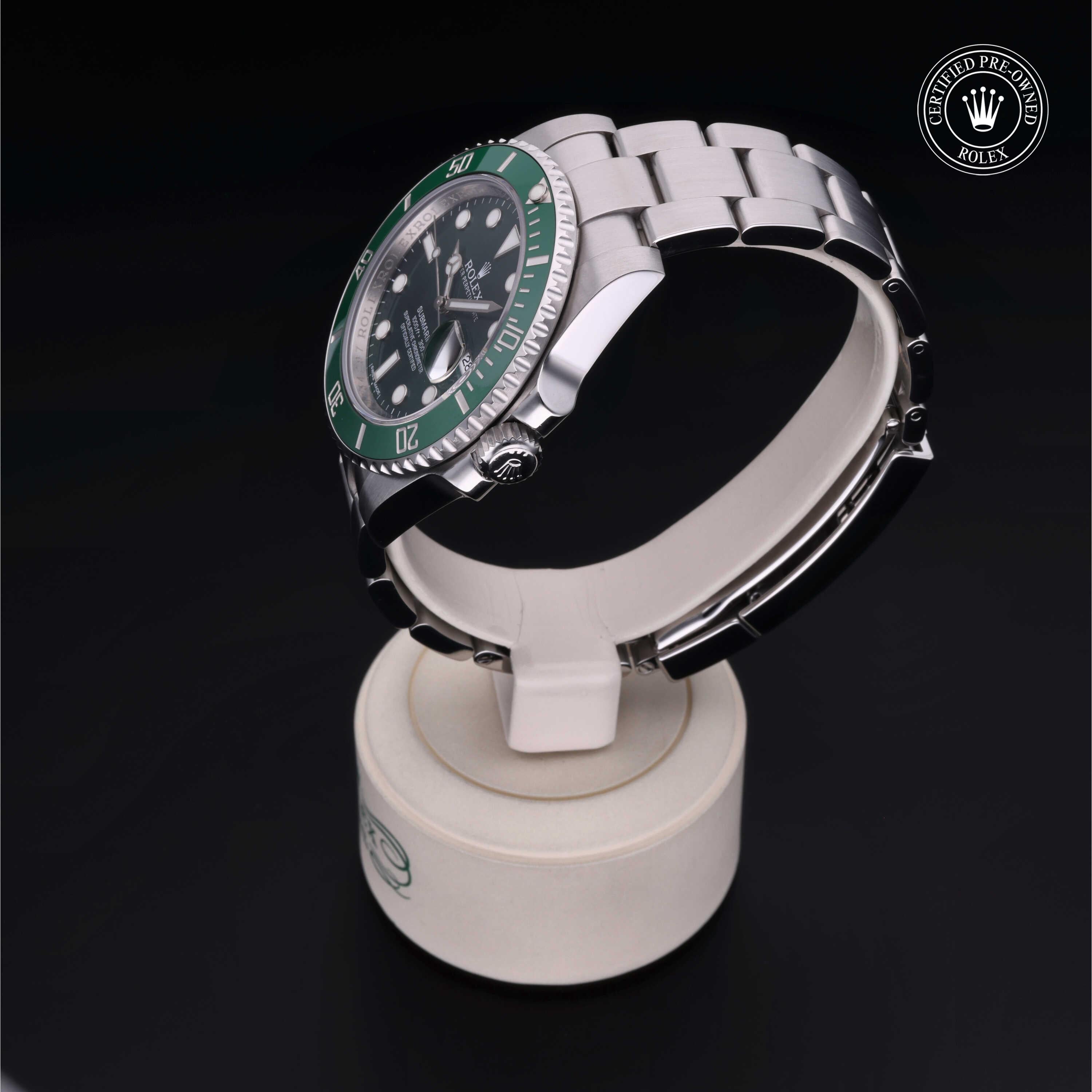 Silver Rolex watch with a green bezel displayed on a white stand against a black background, featuring a certified pre-owned Rolex logo symbolizing luxury and reliability.