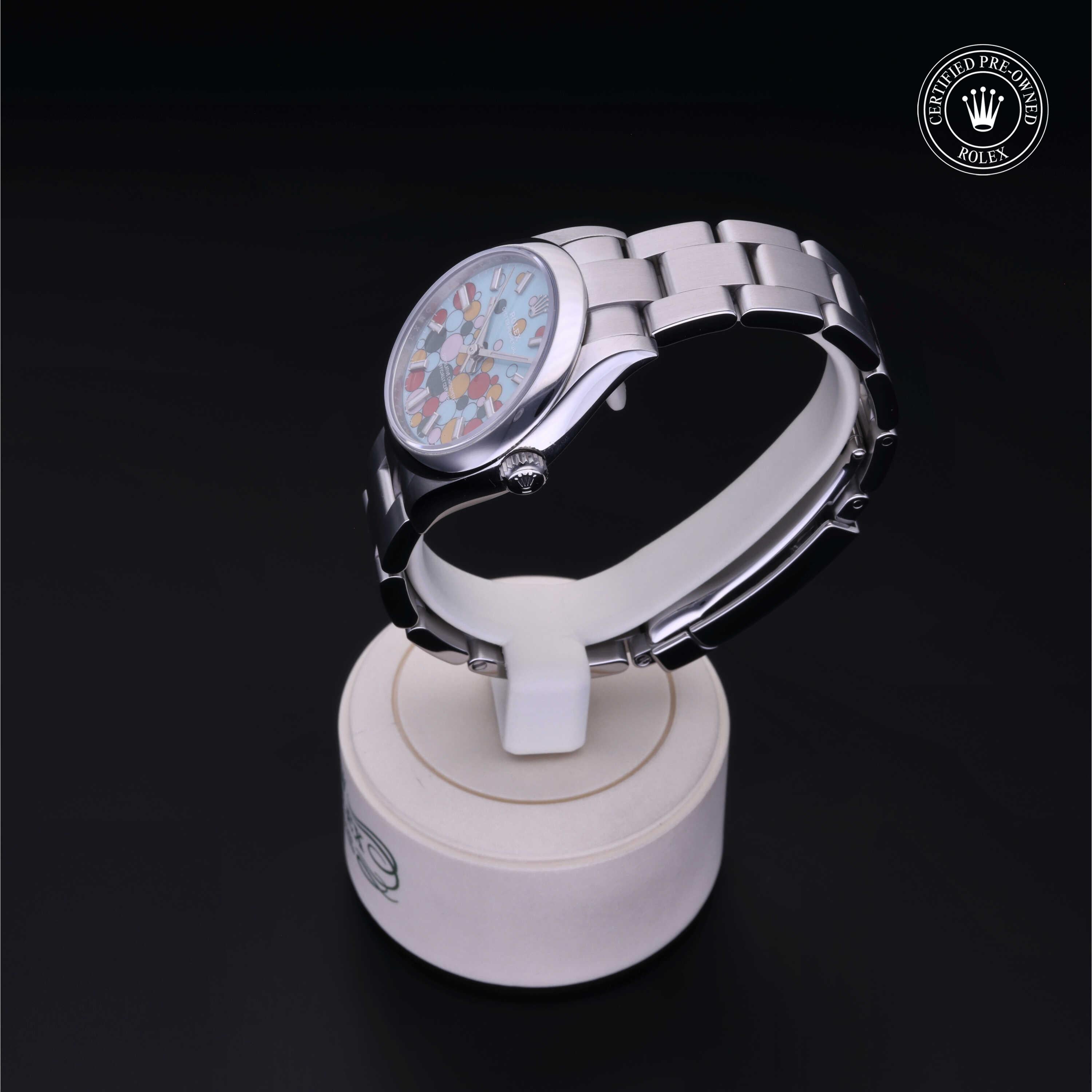 Silver luxury watch with a colorful patterned dial displayed on a white stand against a black background, featuring a Rolex Certified Pre-Owned logo.