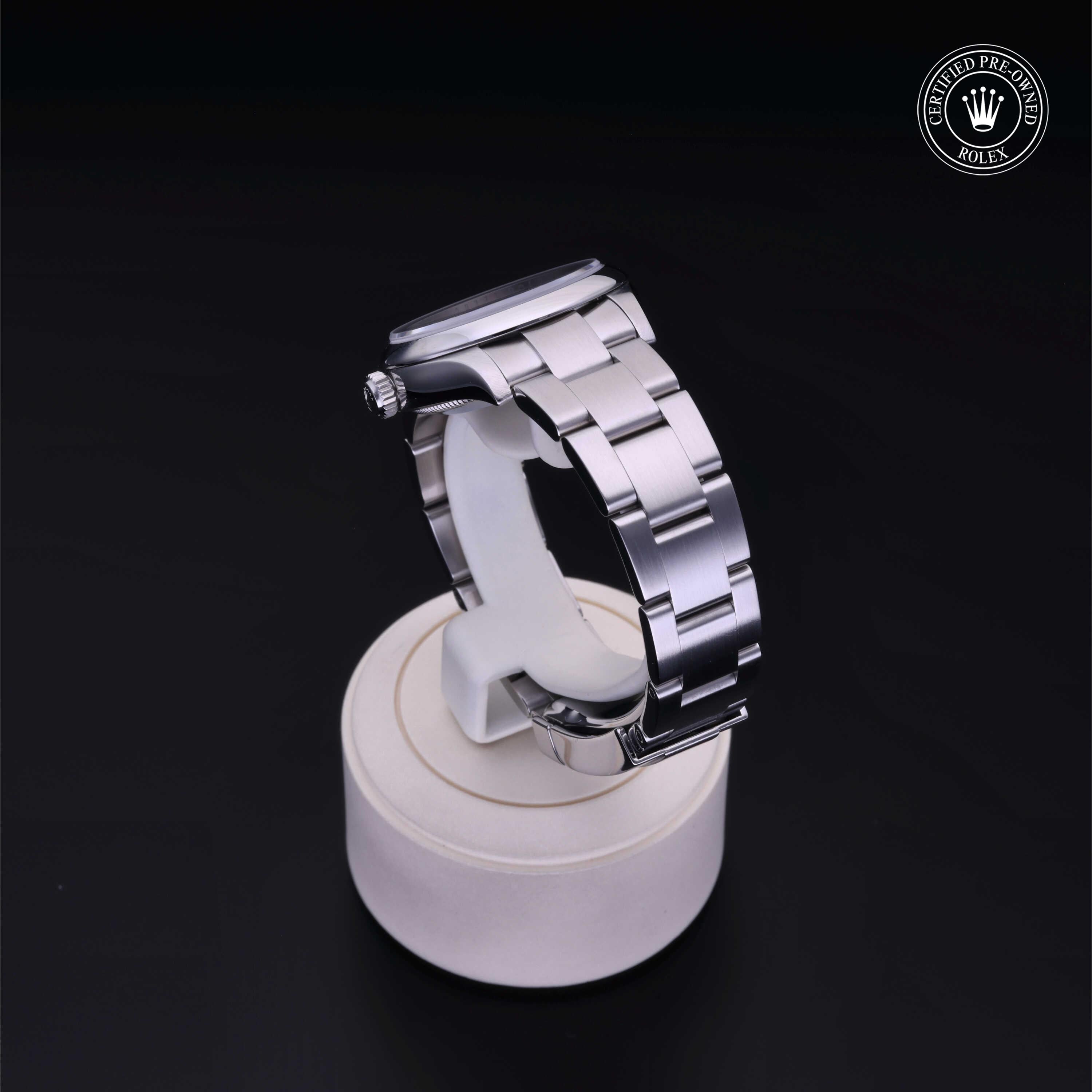 A close-up of a polished silver luxury watch with a metal link bracelet displayed on a white stand against a black background, featuring a certified pre-owned Rolex logo.
